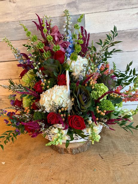 Large mixed flower arrangement with red roses, white hydrangea, and purple accents in a white basket
