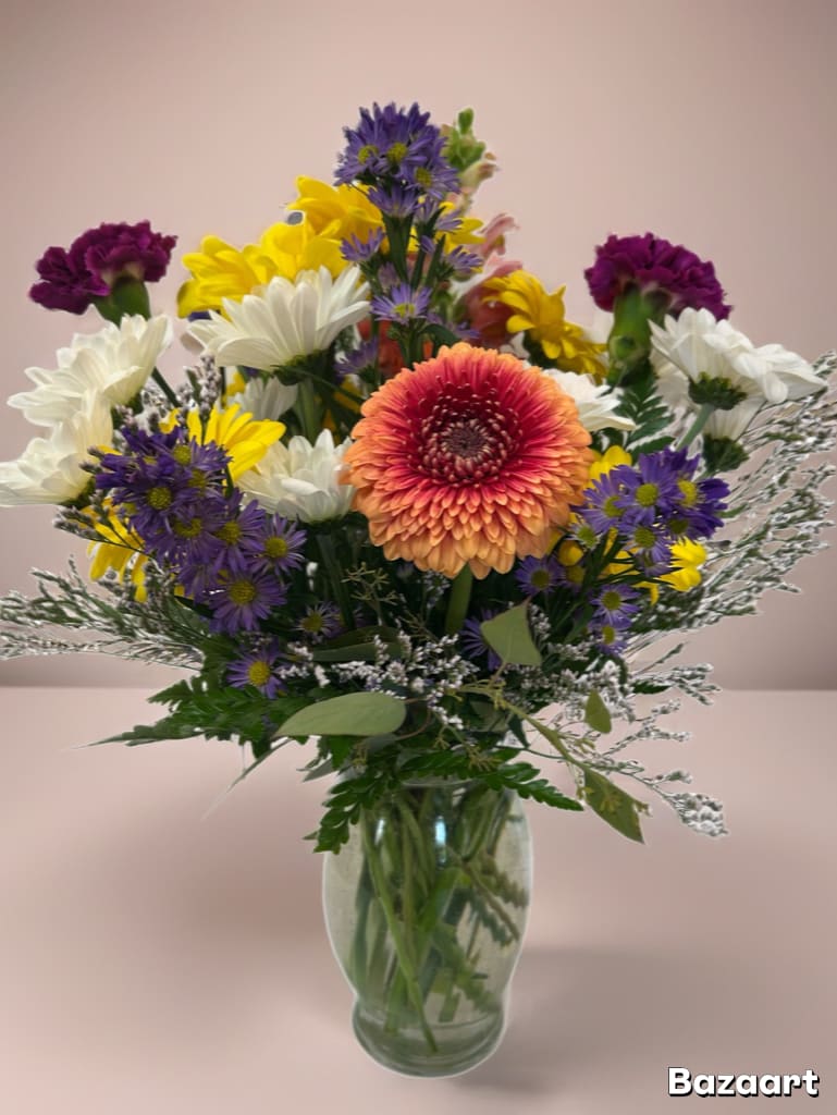 Mixed bouquet in a glass vase with purple, yellow, white, and peach flowers.
