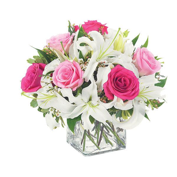 Lovely Lily &amp; Pink Rose Cube - A vision of soft elegance, this floral arrangement is housed in a sleek, crystal-clear cube vase that showcases every detail with modern sophistication. The transparency of the glass allows the stems to become part of the design—neatly trimmed and artfully arranged, they form a natural lattice beneath the blooms.  Emerging from the cube are blush-pink roses, their petals delicately curled like spun silk, radiating warmth and affection. Intertwined among them are graceful pink lilies, their trumpet-shaped blossoms unfurling with gentle drama. The lilies’ subtle speckles and long stamens add texture and movement, while their fragrance lends a sweet, calming aura.  Accents of soft greenery—perhaps sprigs of ruscus or dusty miller—frame the flowers, adding depth without overpowering the pastel palette. The overall effect is fresh, romantic, and timeless.  Perfect for a birthday, anniversary, or simply to say, “you’re loved,” this arrangement turns any space into a moment of beauty.