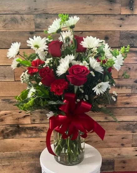 Red roses and white daisies in a glass vase with a red ribbon