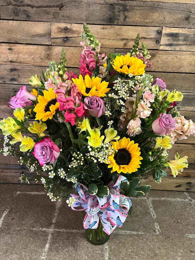 Bouquet of sunflowers, pink roses, and mixed blooms in a glass vase