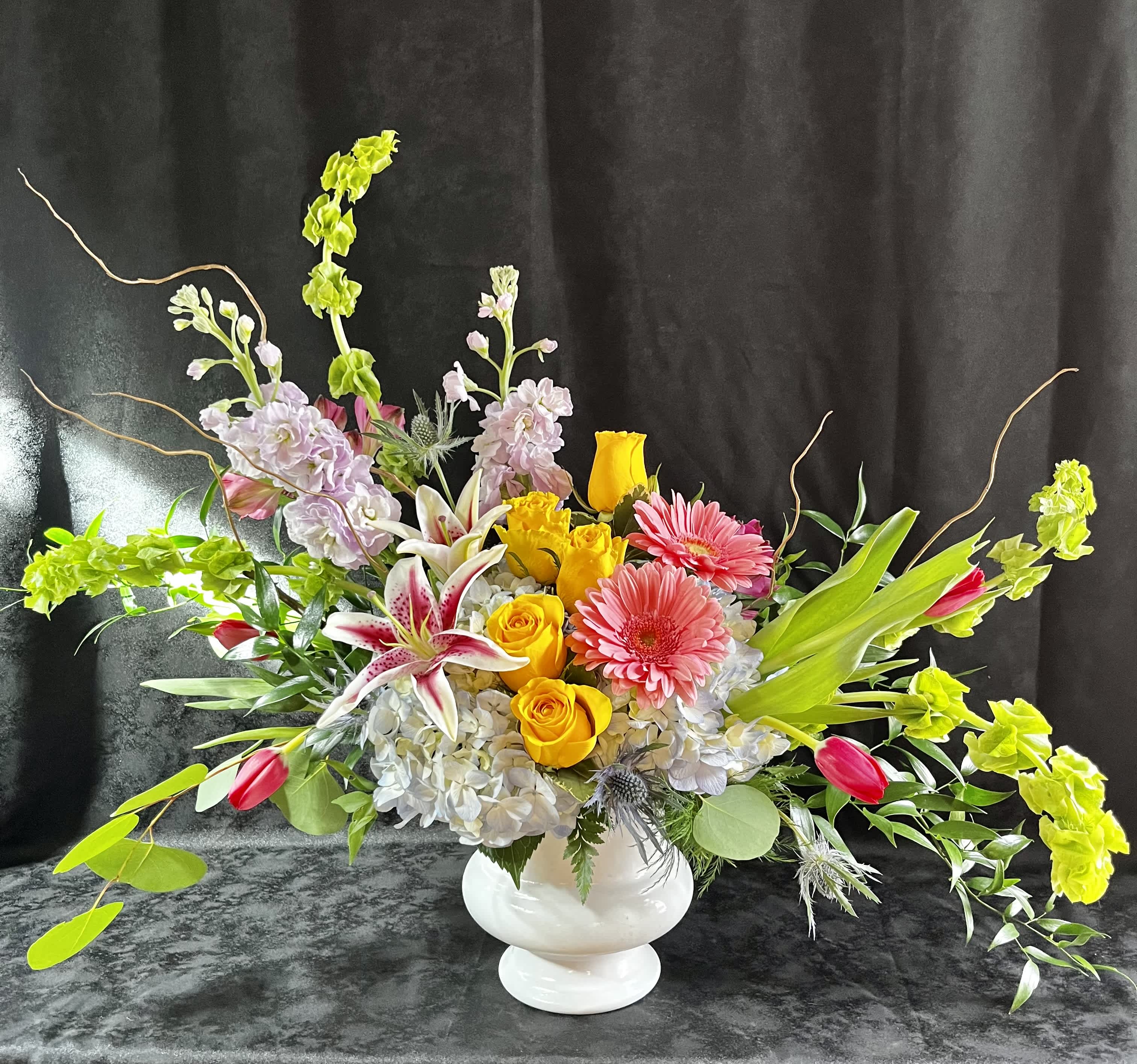 Colorful mixed flower arrangement in a white vase with long branching accents