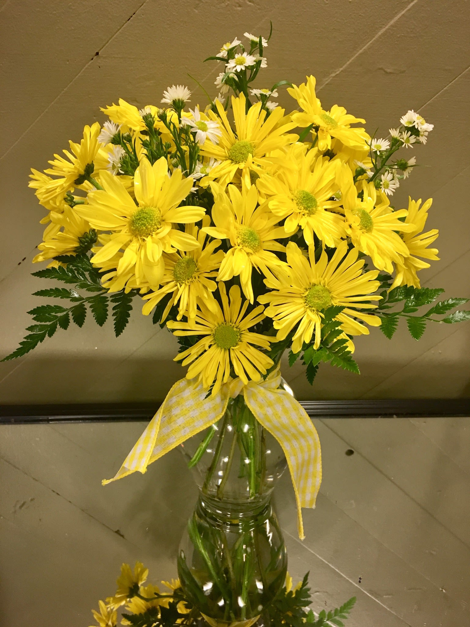 Yellow daisy bouquet in a clear glass vase with a checked ribbon