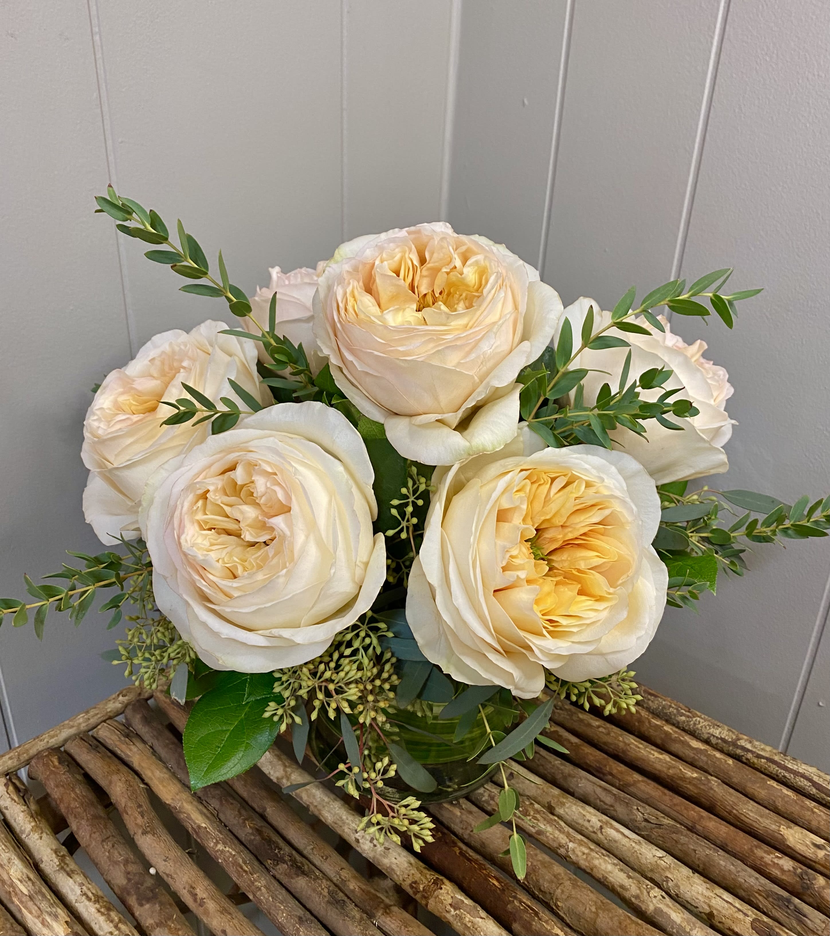Bouquet of cream and pale peach roses with greenery in a glass vase
