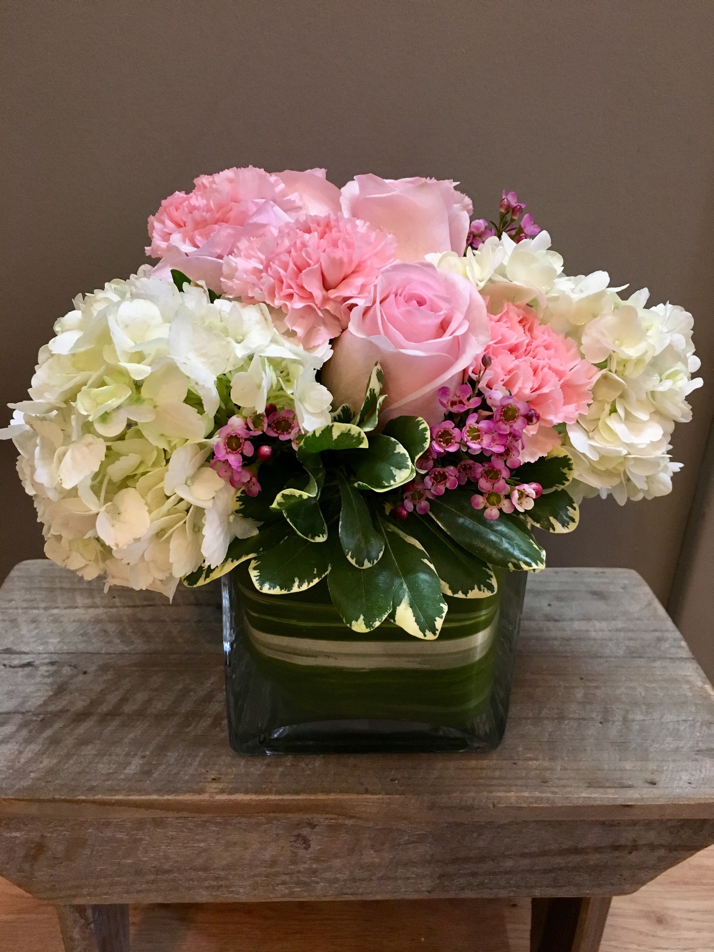 Pink roses and carnations arranged with white hydrangeas in a green glass vase.