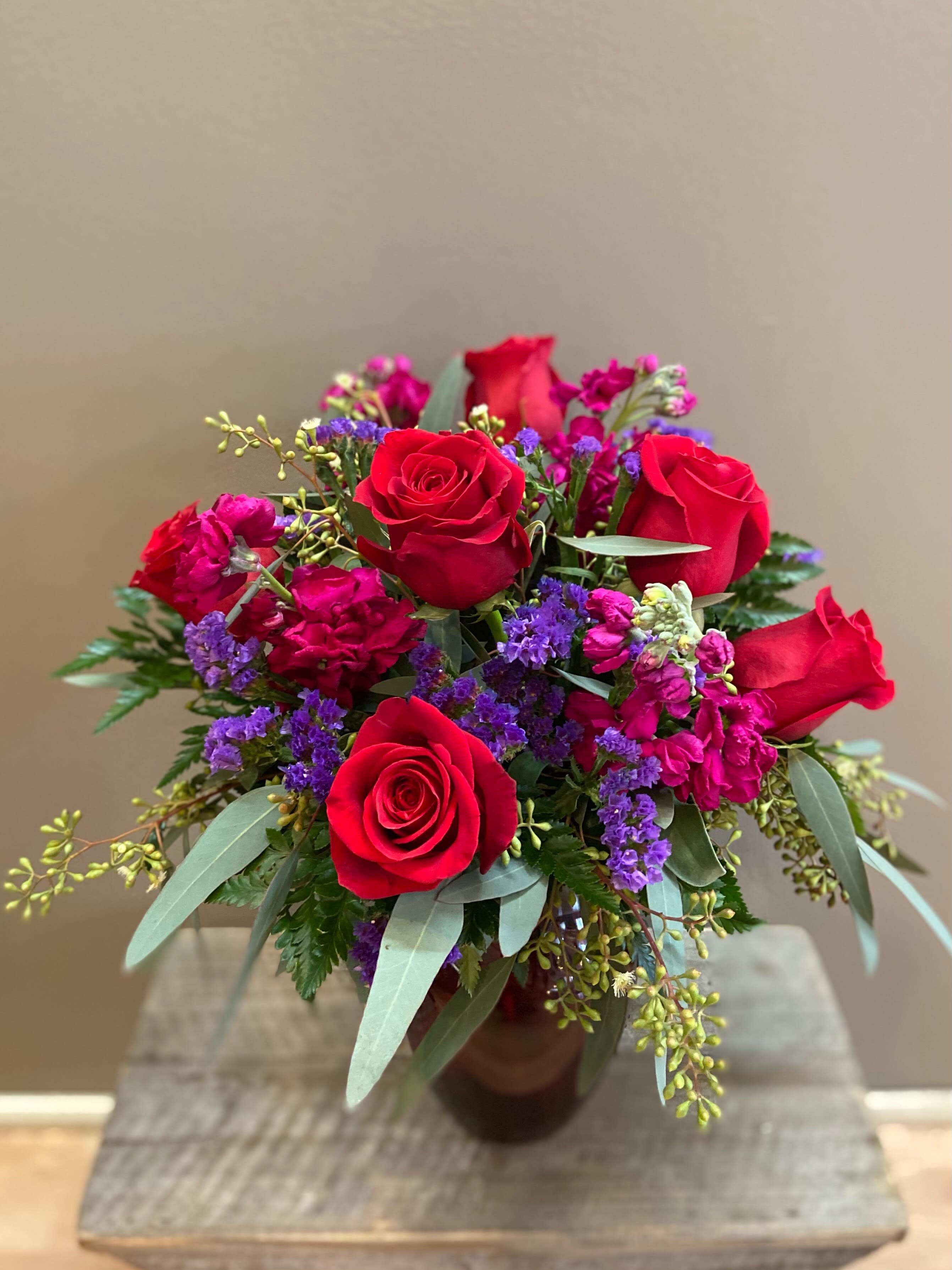 Red Velvet - 6 red roses with stock and statice accented with greenery in a red vase.