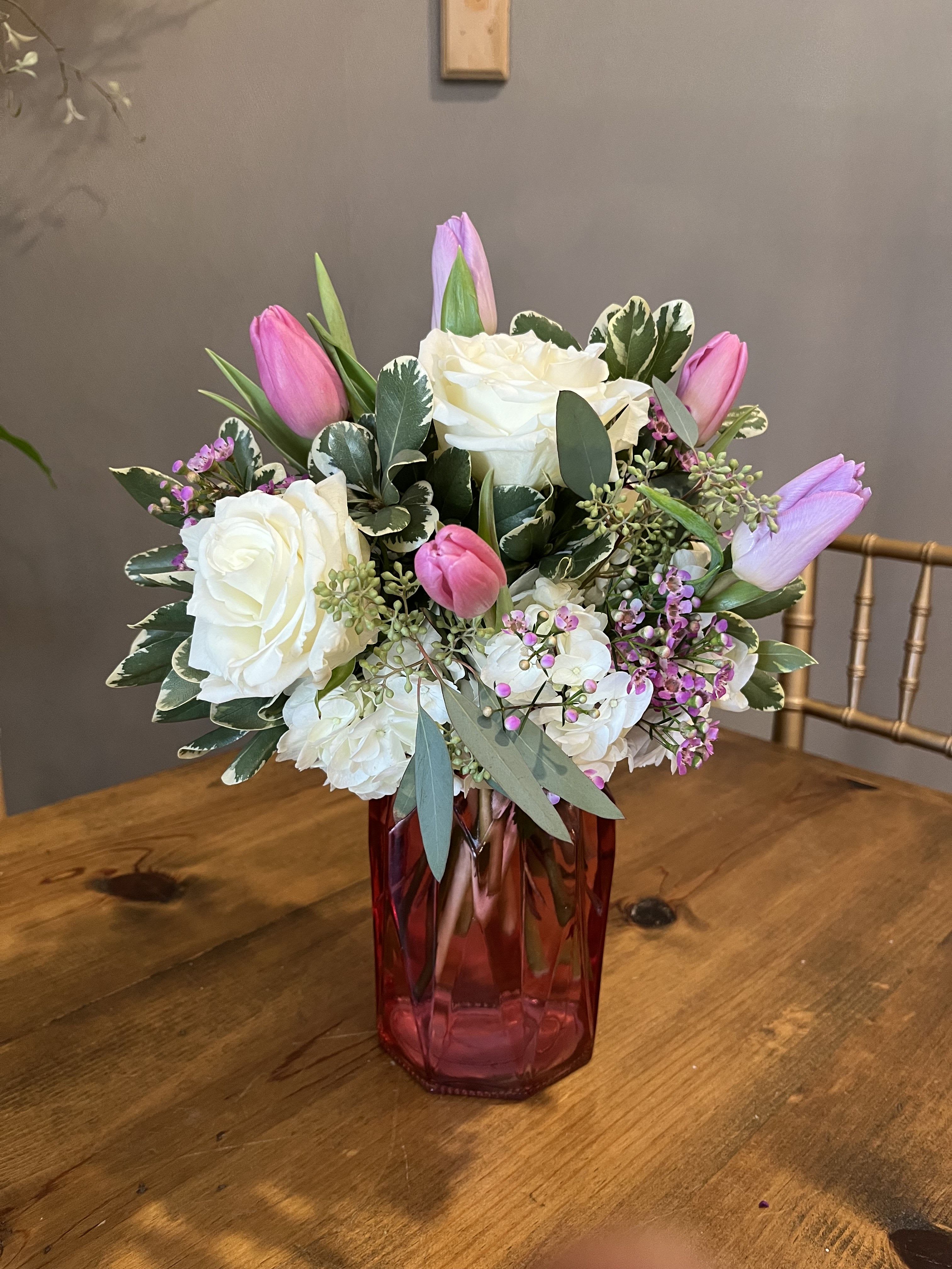 Pink tulips and white roses arranged in a red glass vase