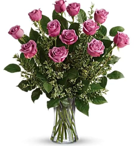 Dozen lavender roses in a clear glass vase with abundant filler foliage