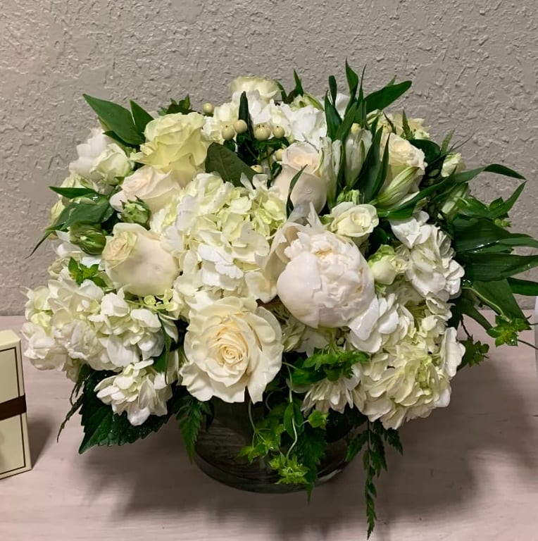Low round arrangement of white roses, hydrangeas, and peonies in a glass vase