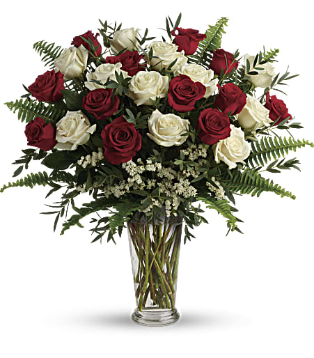 Tall arrangement of red and white roses with ferns in a clear glass vase