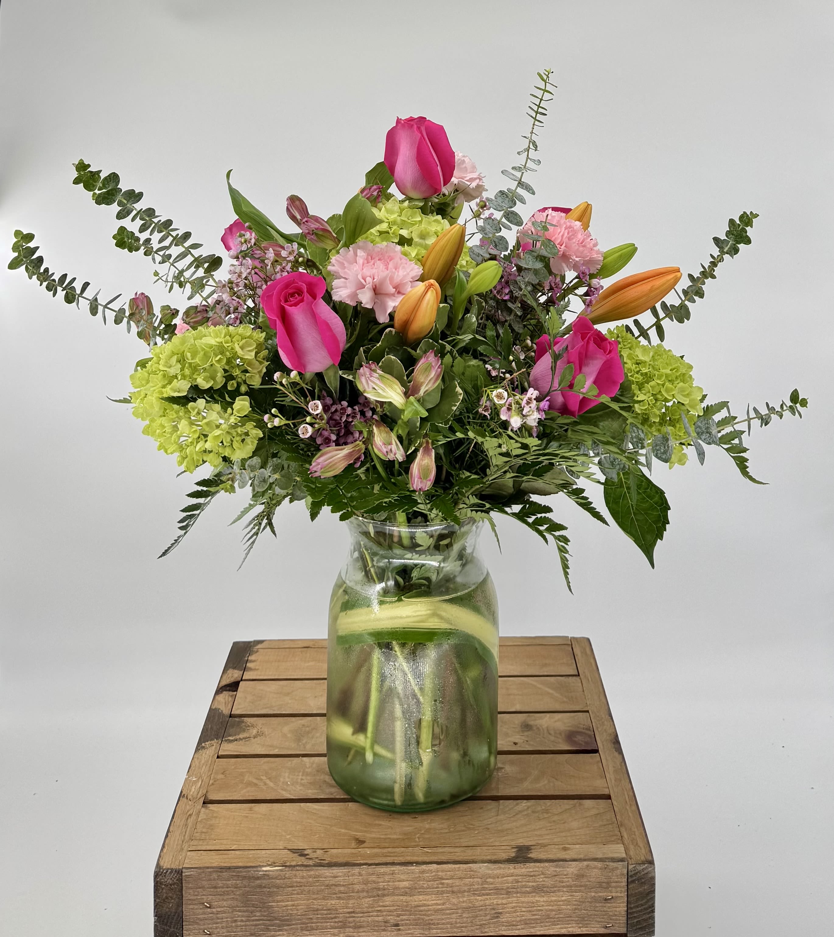 Mixed bouquet of pink roses, orange lilies, and green hydrangeas in a clear glass jar vase