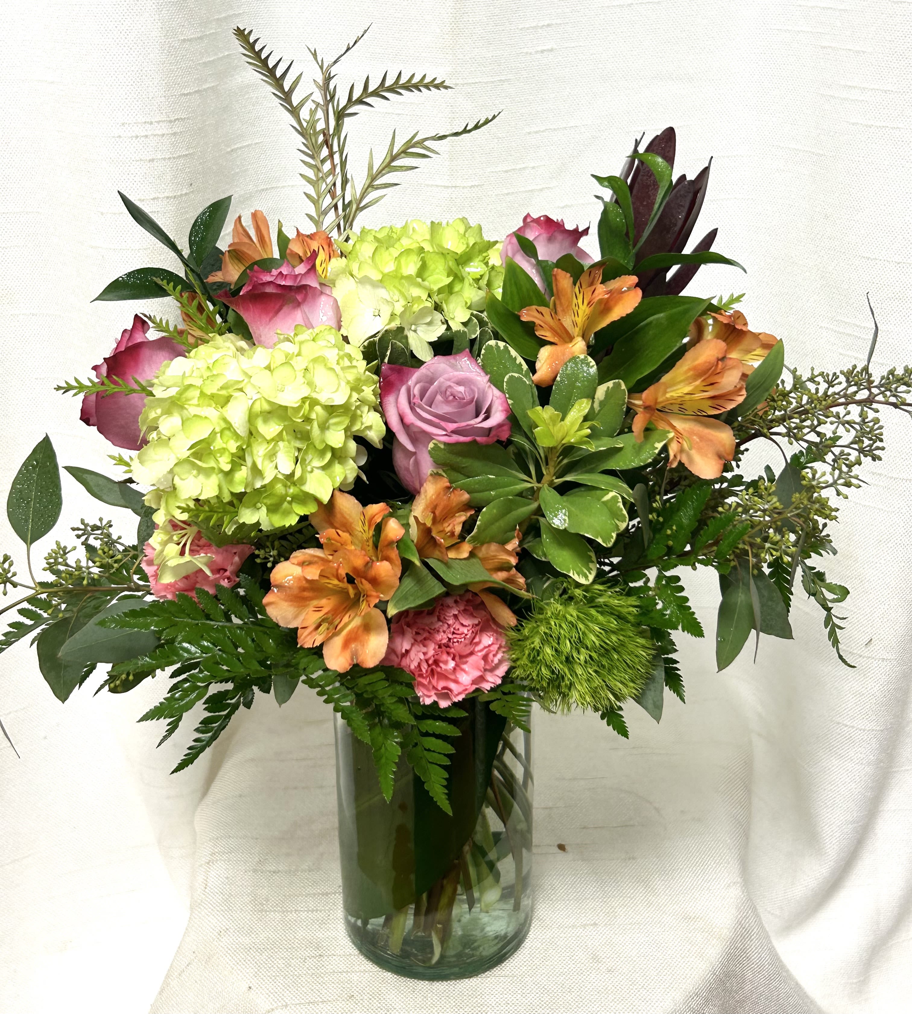 Mixed bouquet of green hydrangeas, pink roses and carnations, and orange alstroemeria in a glass vase