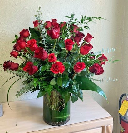 Tall arrangement of red roses with lush foliage in a clear glass cylinder vase