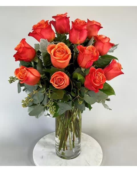 Arrangement of orange roses in a clear glass vase on a round white table