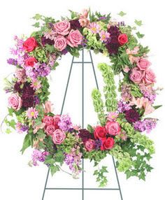 Standing wreath of pink and red roses with mixed purple flowers on a metal easel
