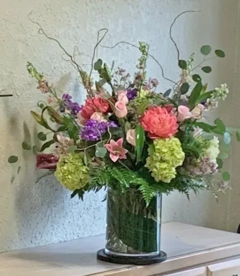 Tall mixed arrangement of pink, green, and purple flowers in a clear glass cylinder vase