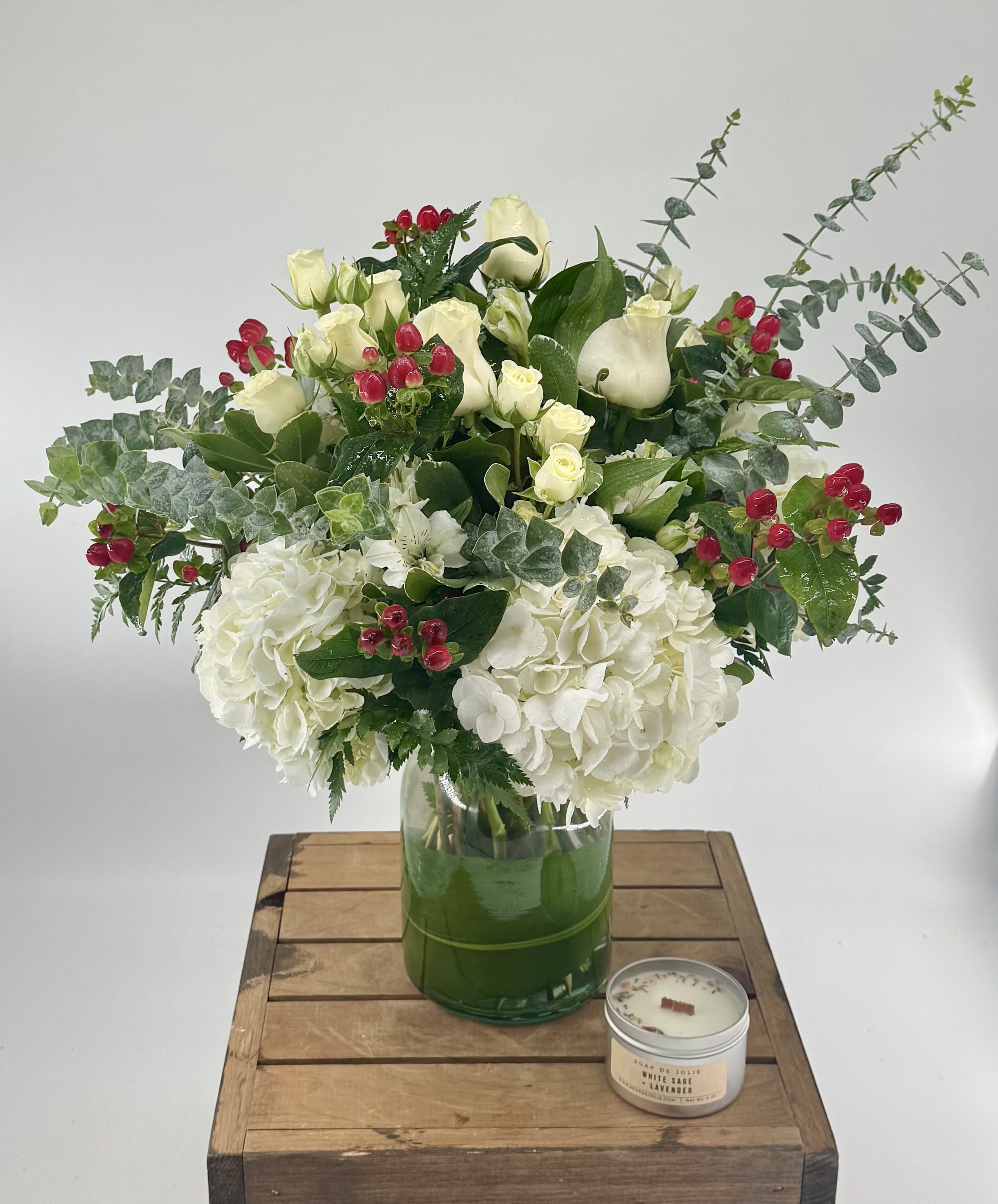 White floral arrangement in a glass vase with red berry accents