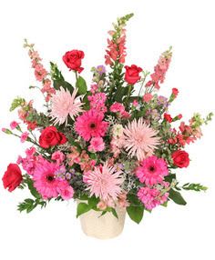 Pink and red mixed flower arrangement in a cream ceramic container