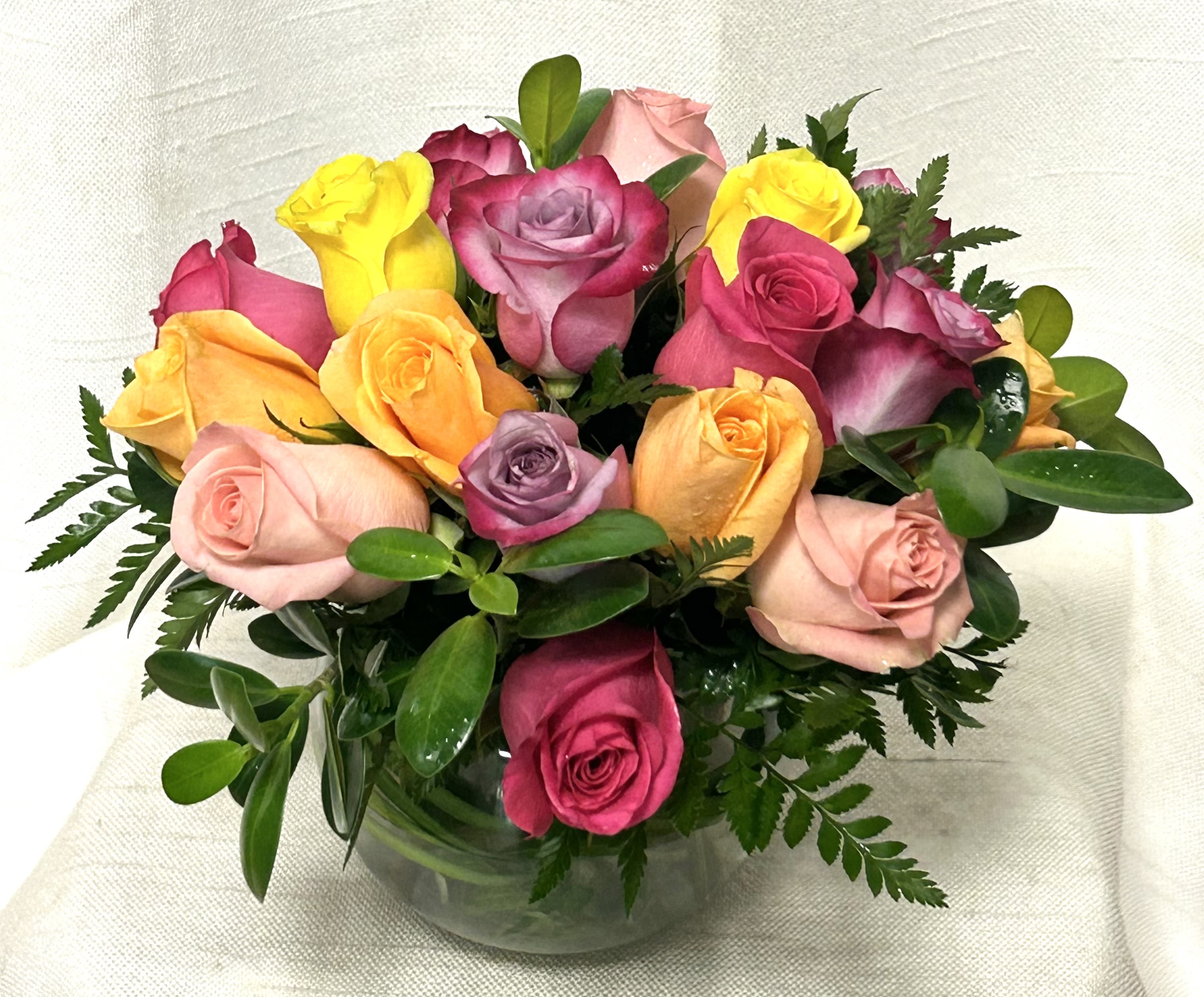 Low round arrangement of mixed-color roses in a clear glass bowl vase