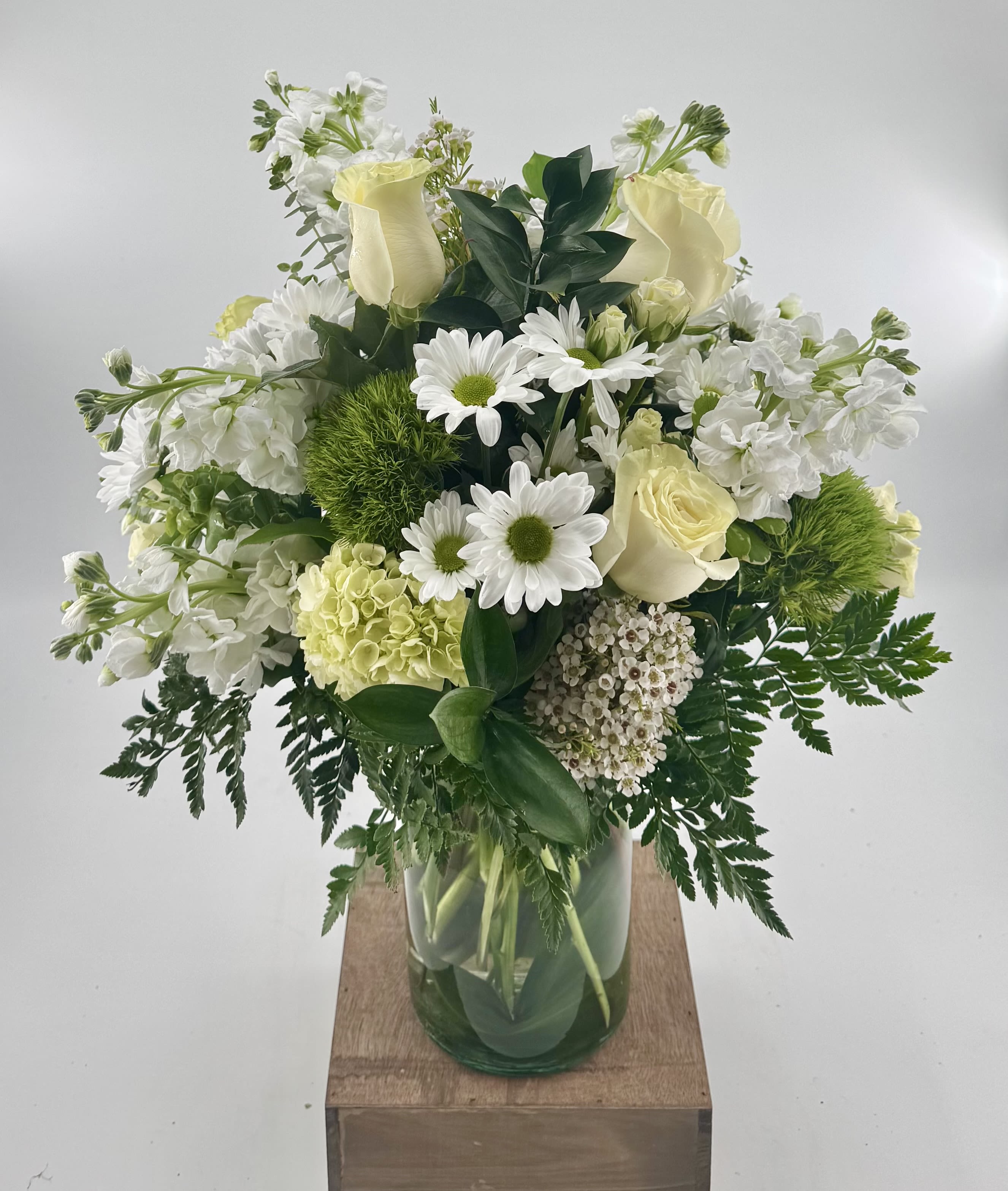 White and cream bouquet with roses, daisies, hydrangea, and green dianthus in a clear glass vase