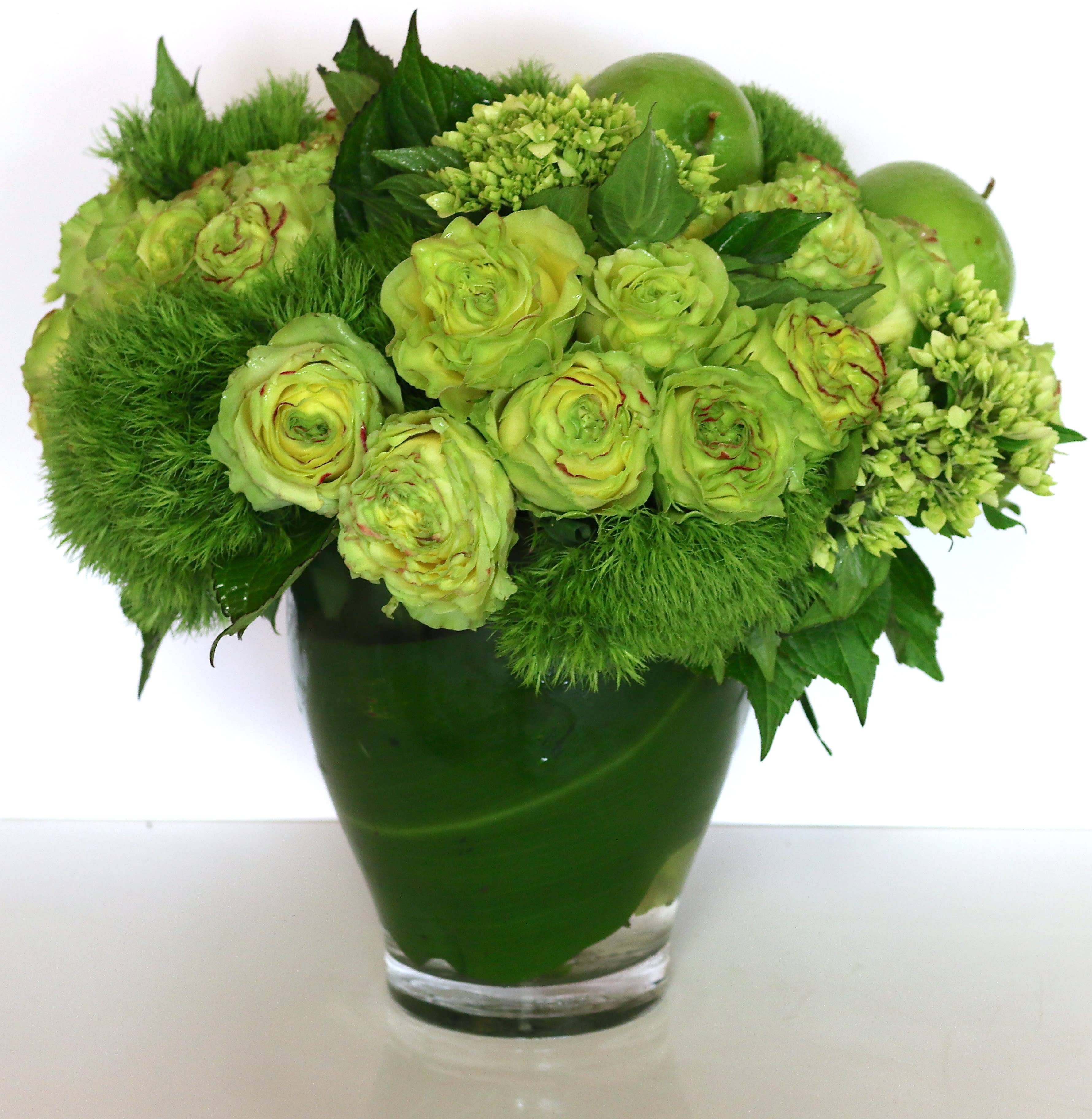 Monochromatic green arrangement with roses and apples in a clear glass vase
