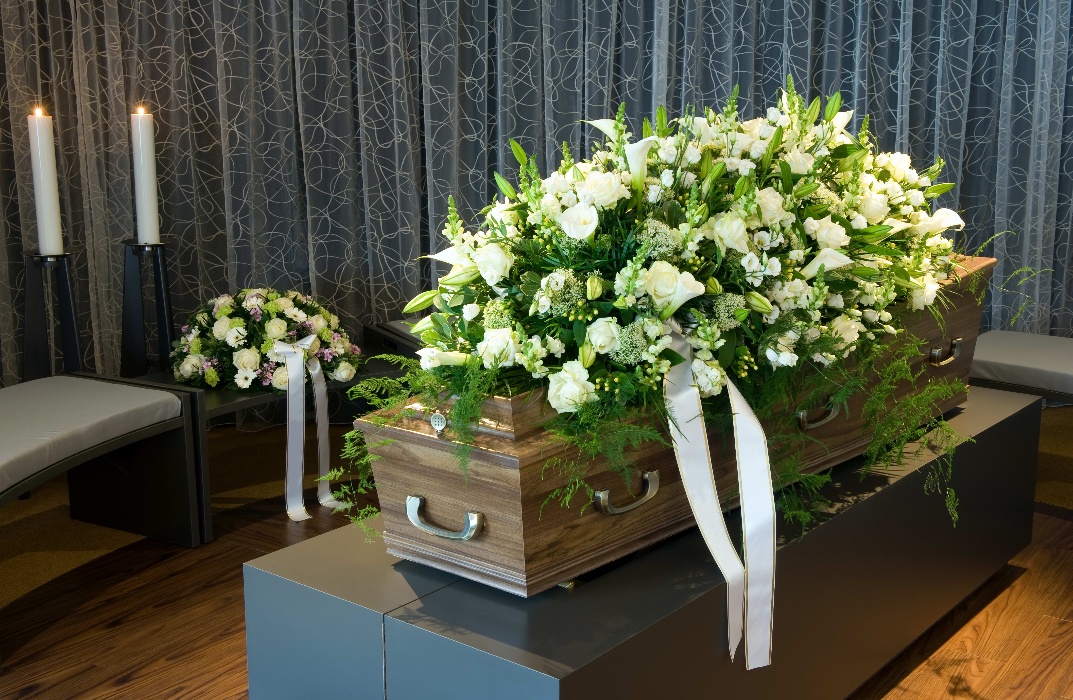 Large white and green casket spray of roses and lilies with ribbons on a wooden casket in a funeral setting