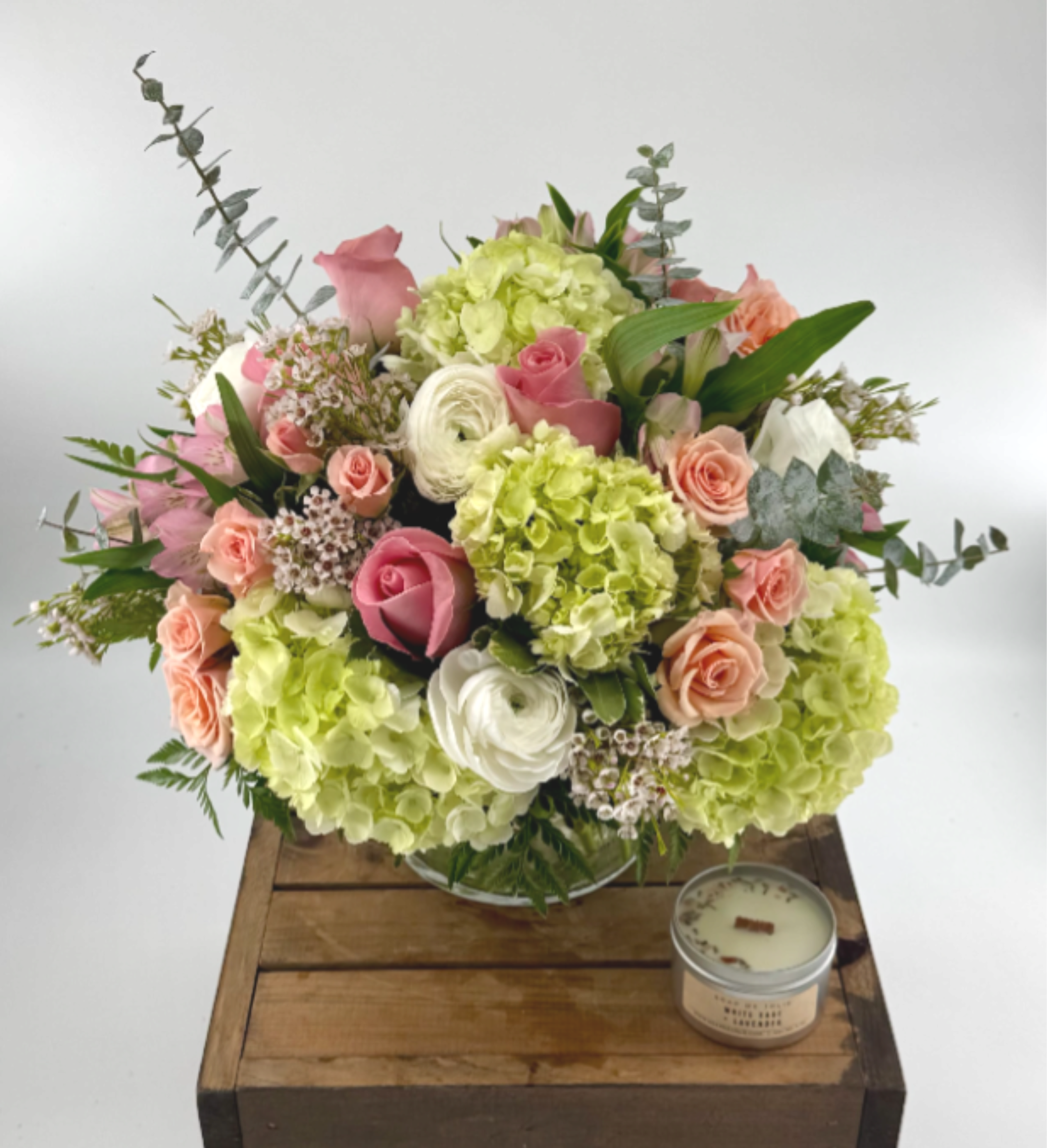 Simplicity (BR) - Delight in a stunning blend of green and white hydrangea, white or pink ranunculus, roses, alstroemeria,wax flower and eucalyptus, artfully arranged in a leaf-lined 6x6” clear vase—crafted to elevate your most cherished moments. 