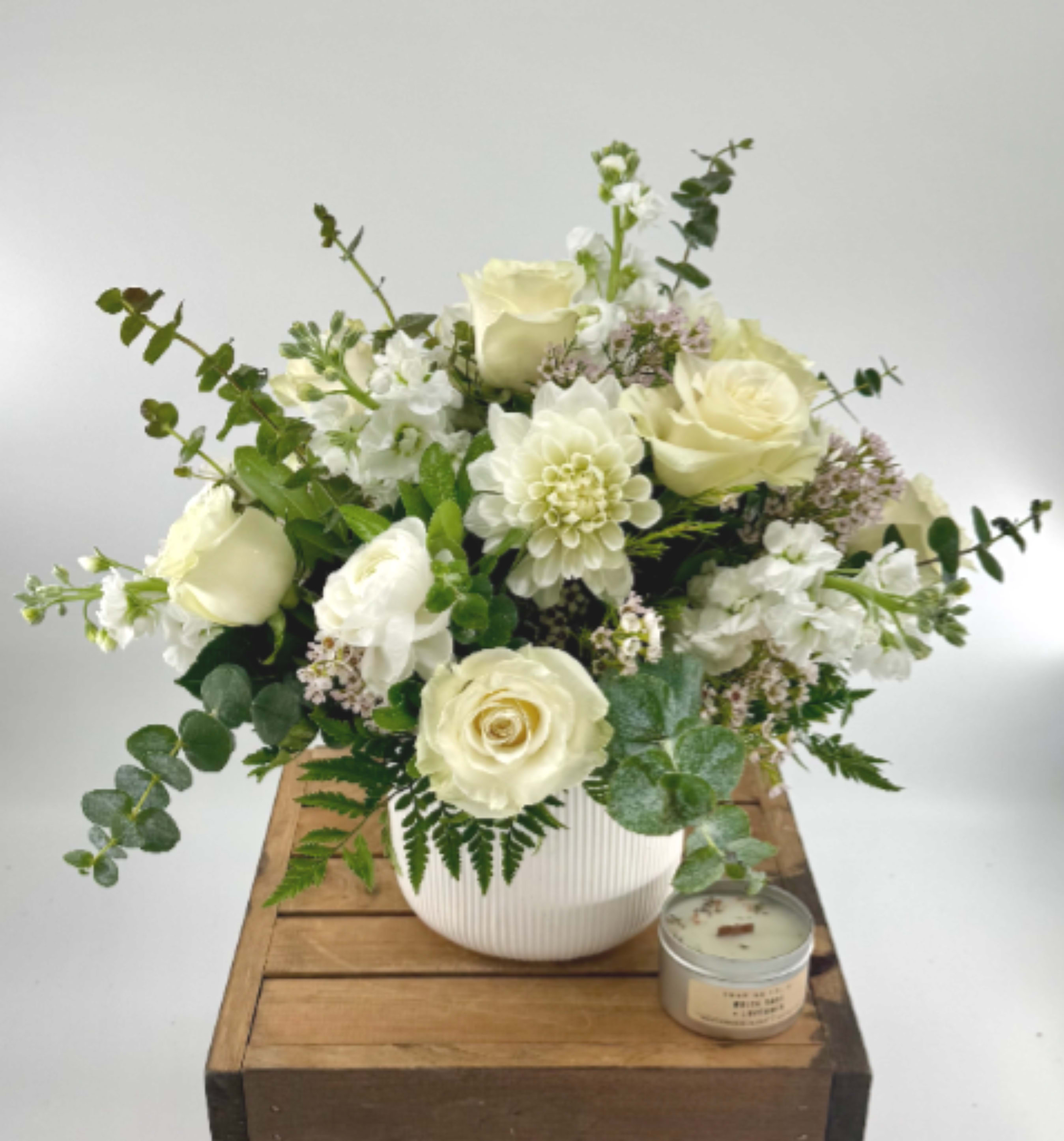 Cream rose and white flower arrangement in a white vase with a candle