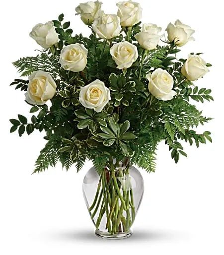 White roses with abundant greenery arranged in a clear glass vase