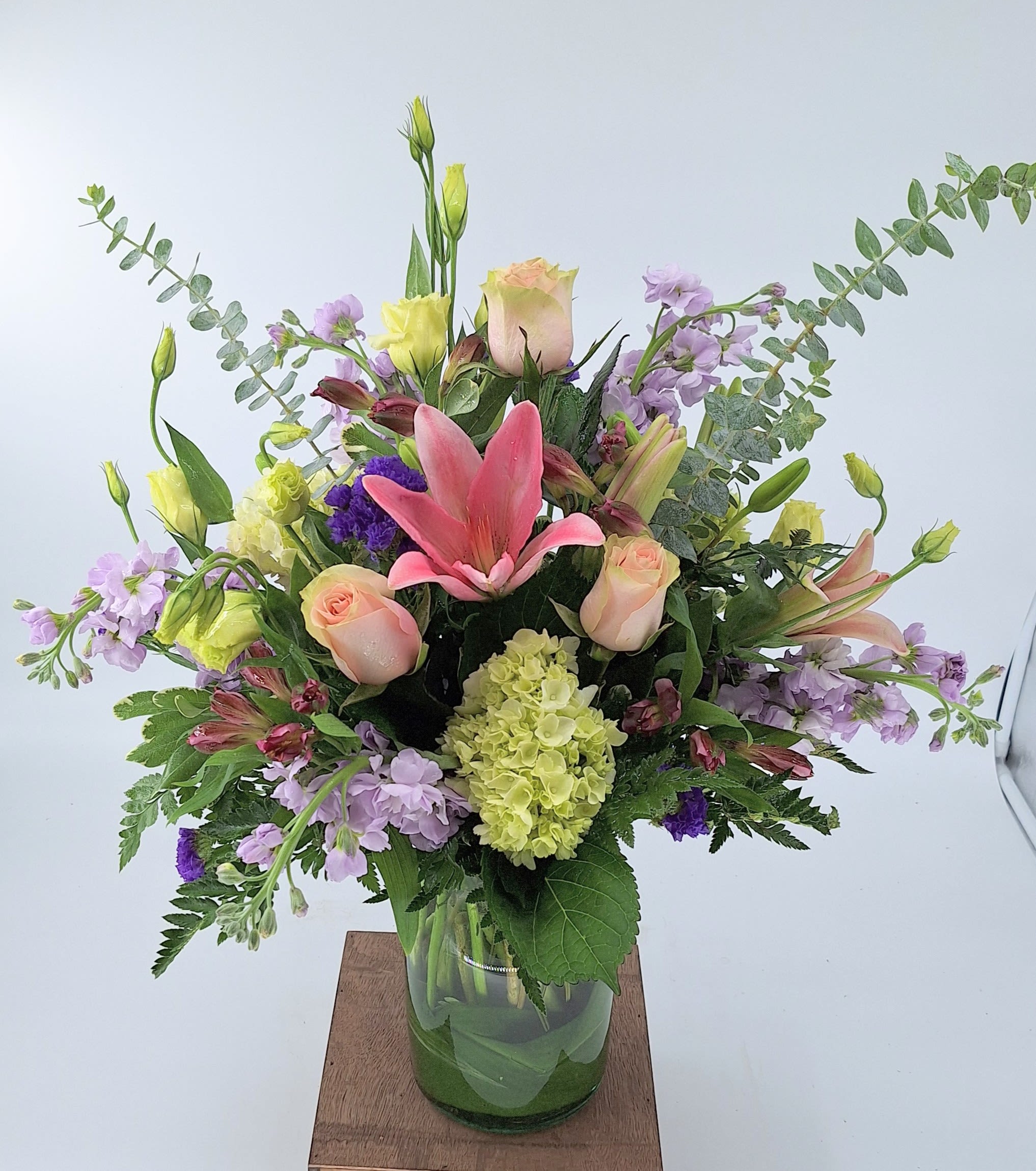 Mixed arrangement of pink lilies, roses, and pastel flowers in a clear glass vase