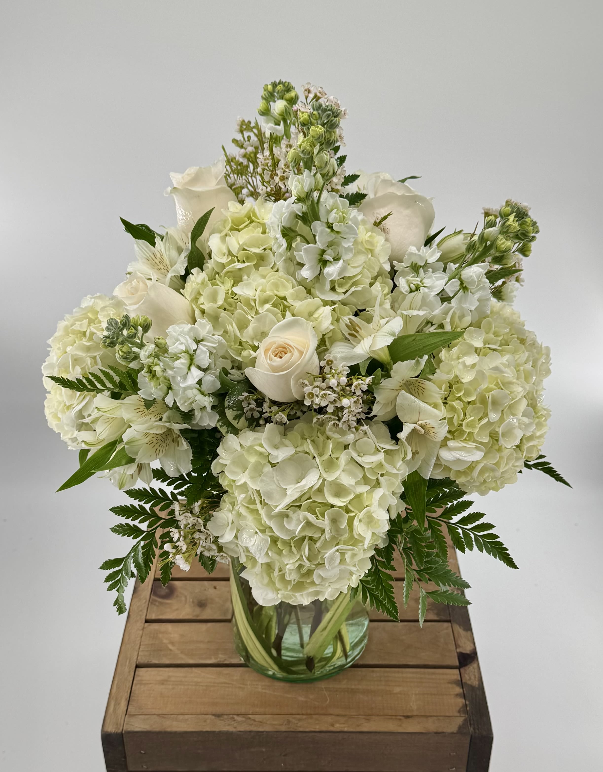 Our Anniversary (DL) - Celebrate your anniversary in style with our modern all-white flower arrangement. This stunning arrangement features a pristine combination of roses, hydrangea, and stock, expertly arranged in a sleek glass vase.