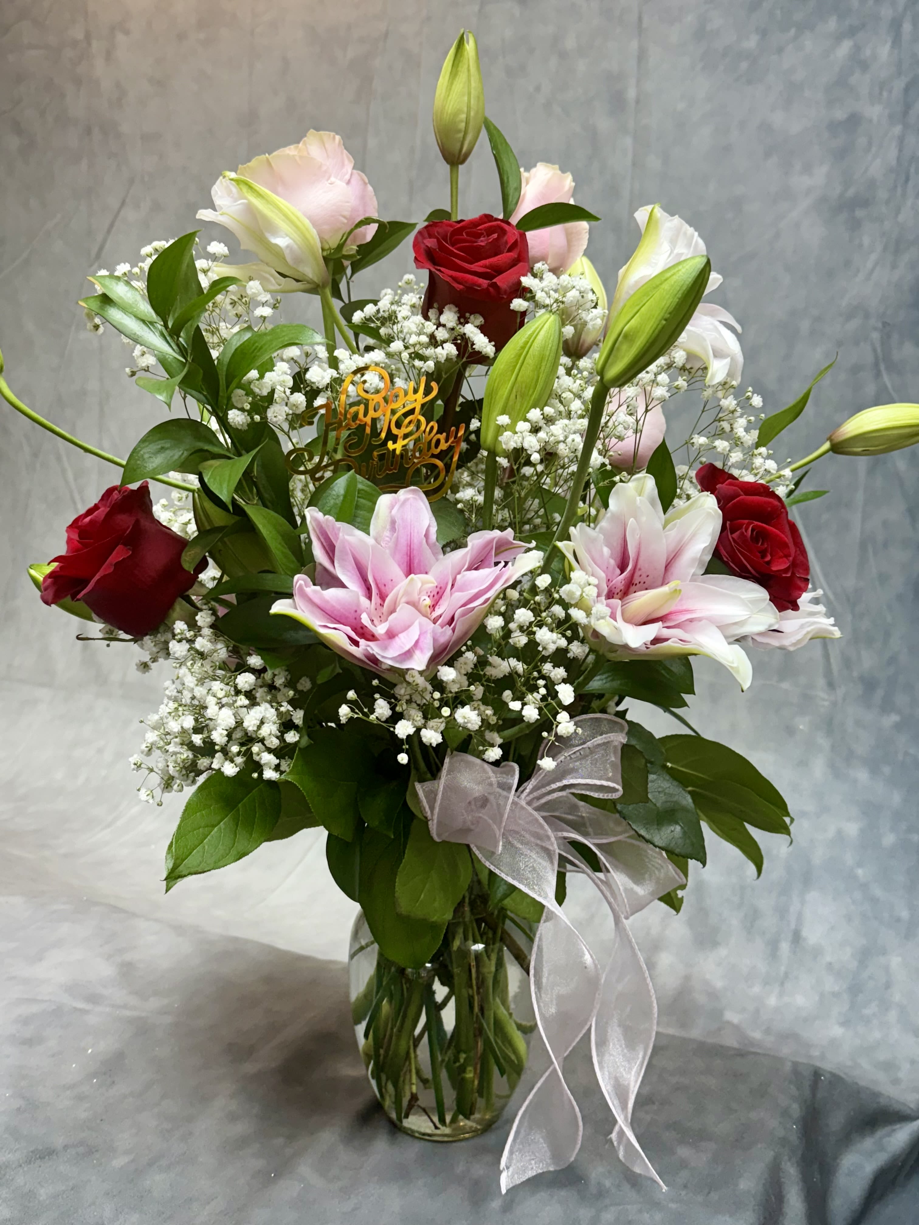 Mixed bouquet of red roses, pink lilies, and white baby's breath in a glass vase
