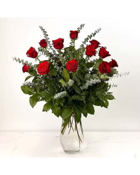 Red roses arranged in a clear glass vase with eucalyptus