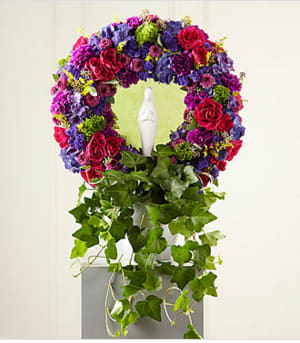 The FTD® Faith &amp; Understanding™ Wreath (DL) - This variation on the traditional sympathy wreath includes brilliant, jewel-toned blossom. This impressive wreath, handcrafted of hot pink spray roses, purple statice and hydrangeas and magenta button pompons. It makes a beautiful tribute to a life of faith and is an excellent choice for a wake or funeral service.   Statue not included