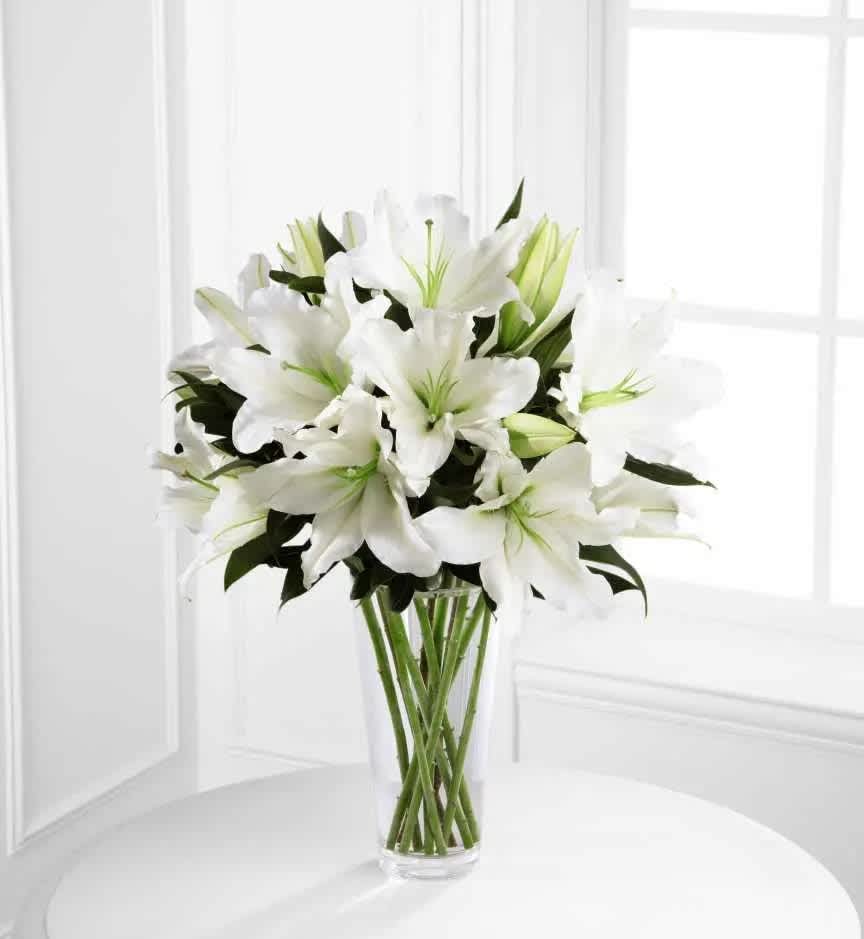 Light in Your Honor (DL) - Our funeral arrangement in a clear glass vase containing all white lilies is a stunning tribute to the memory of your loved one. The lilies offer a simple, yet elegant display that is both pure and calming, as white is often associated with purity and innocence.  