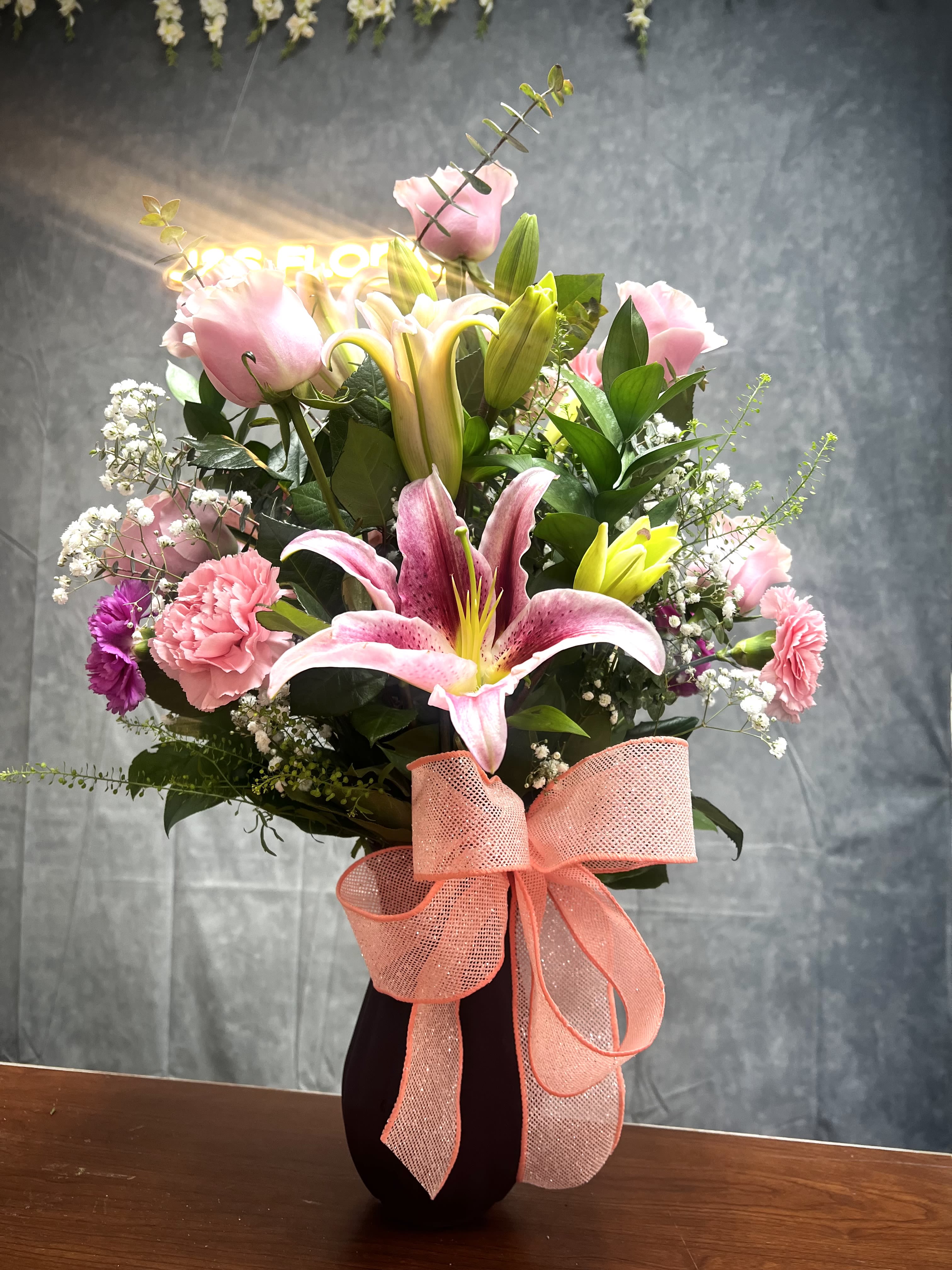 Pink lilies and carnations in a dark vase with a peach ribbon