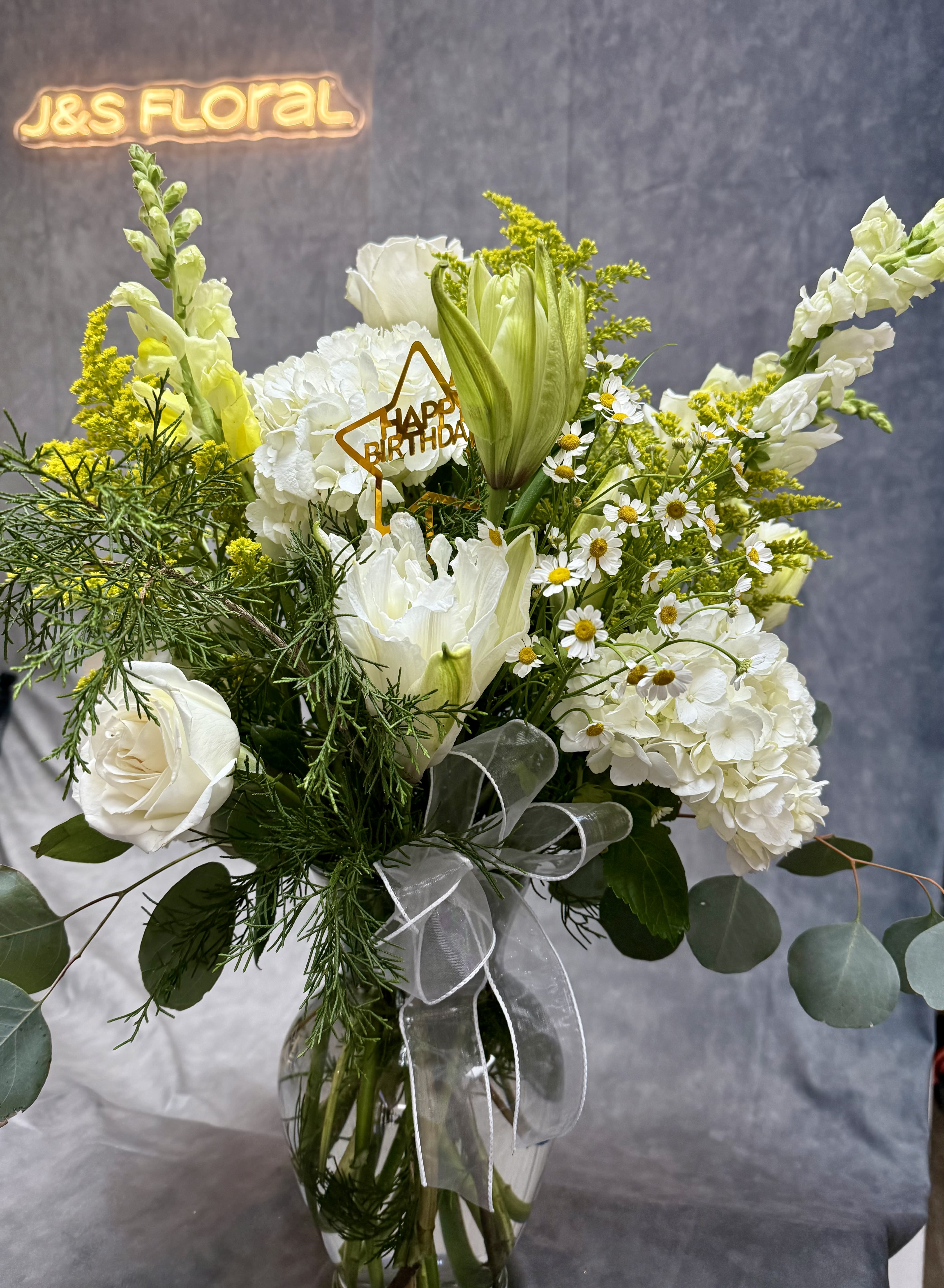 White floral bouquet in a glass vase with a birthday pick