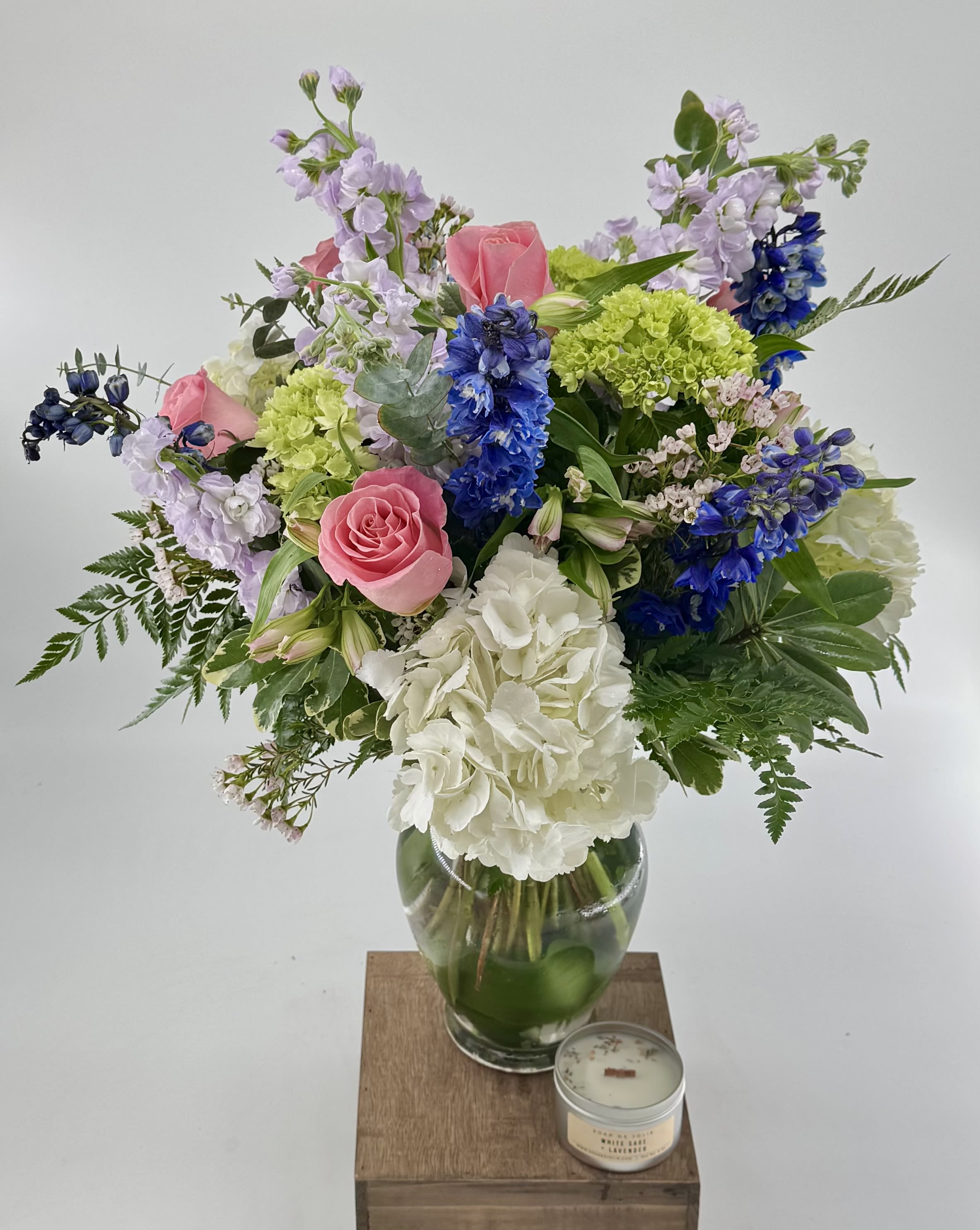 Mixed bouquet of pink roses, white hydrangea, and blue flowers in a glass vase