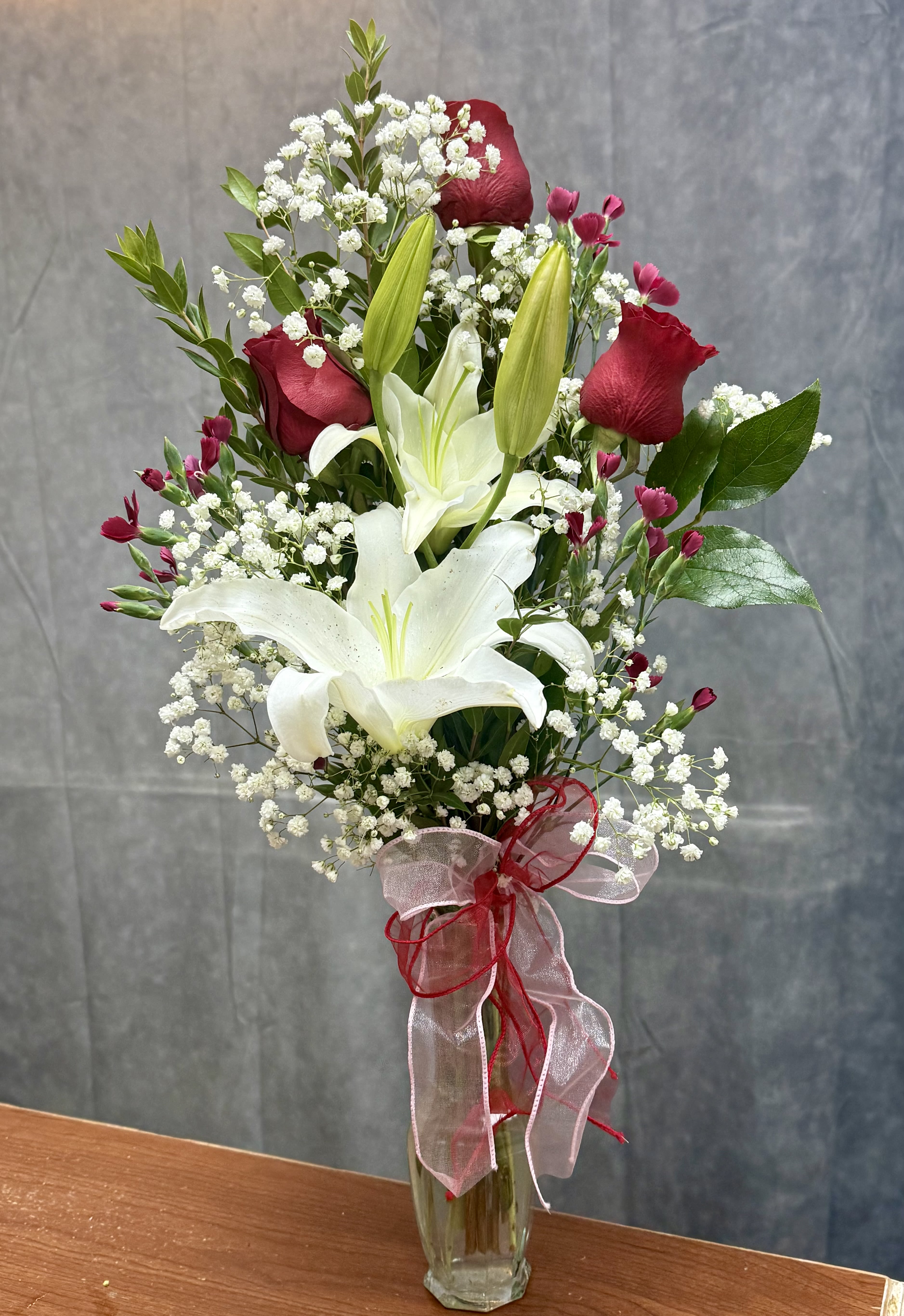 Tall bouquet of white lilies and red roses in a glass vase