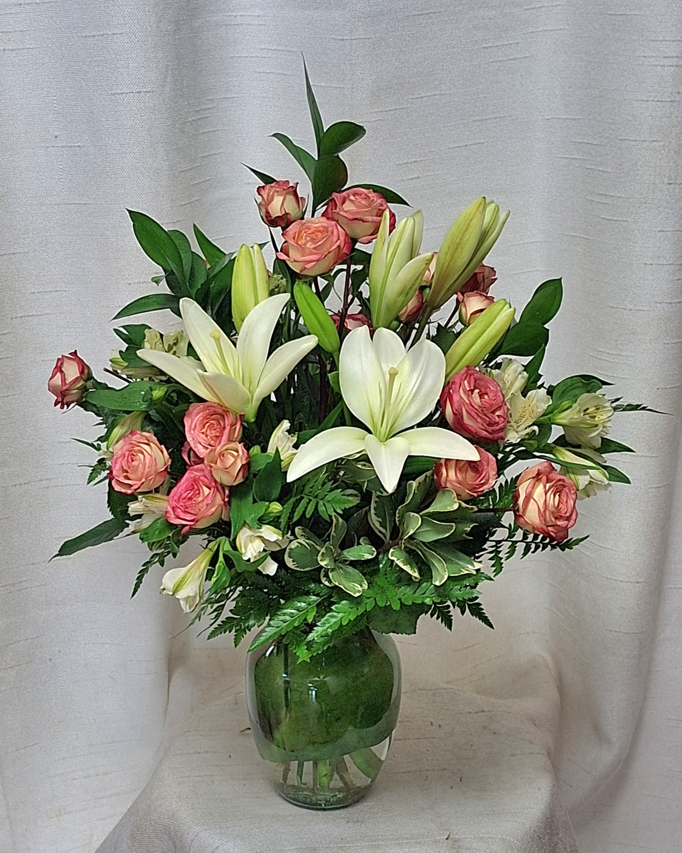 In Style (DL) - Introducing a stunning flower arrangement that exudes elegance and charm. This exquisite bouquet features a delicate blend of soft pink roses, white lilies, white daisies, and white alstroemeria, expertly arranged in a glass vase with lush greenery and filler for a touch of natural beauty.  