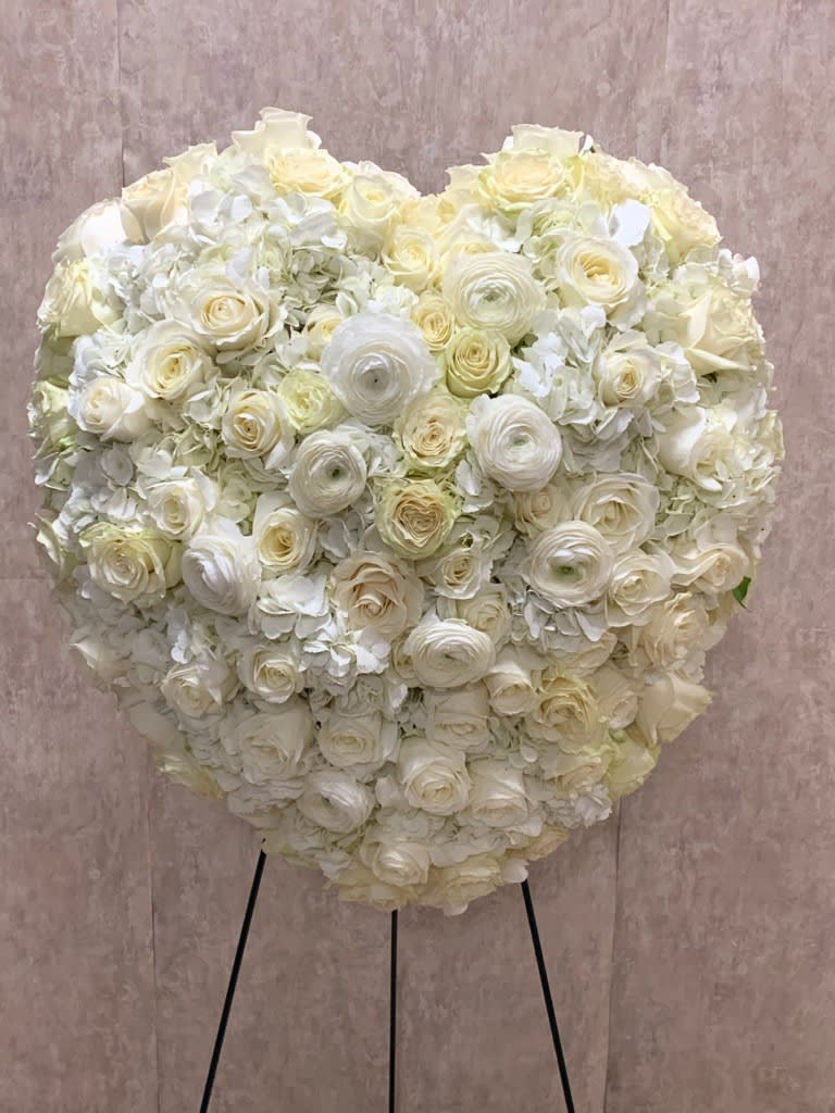 Heavy Heart Standing Spray (BB) - Create a heartfelt tribute to honor the memory of a loved one with our closed heart spray. This elegant arrangement features a bed of pristine white roses and delicate white ranunculus, perfectly arranged in the shape of a closed heart. It serves as a beautiful and meaningful symbol of love, remembrance, and eternal peace.