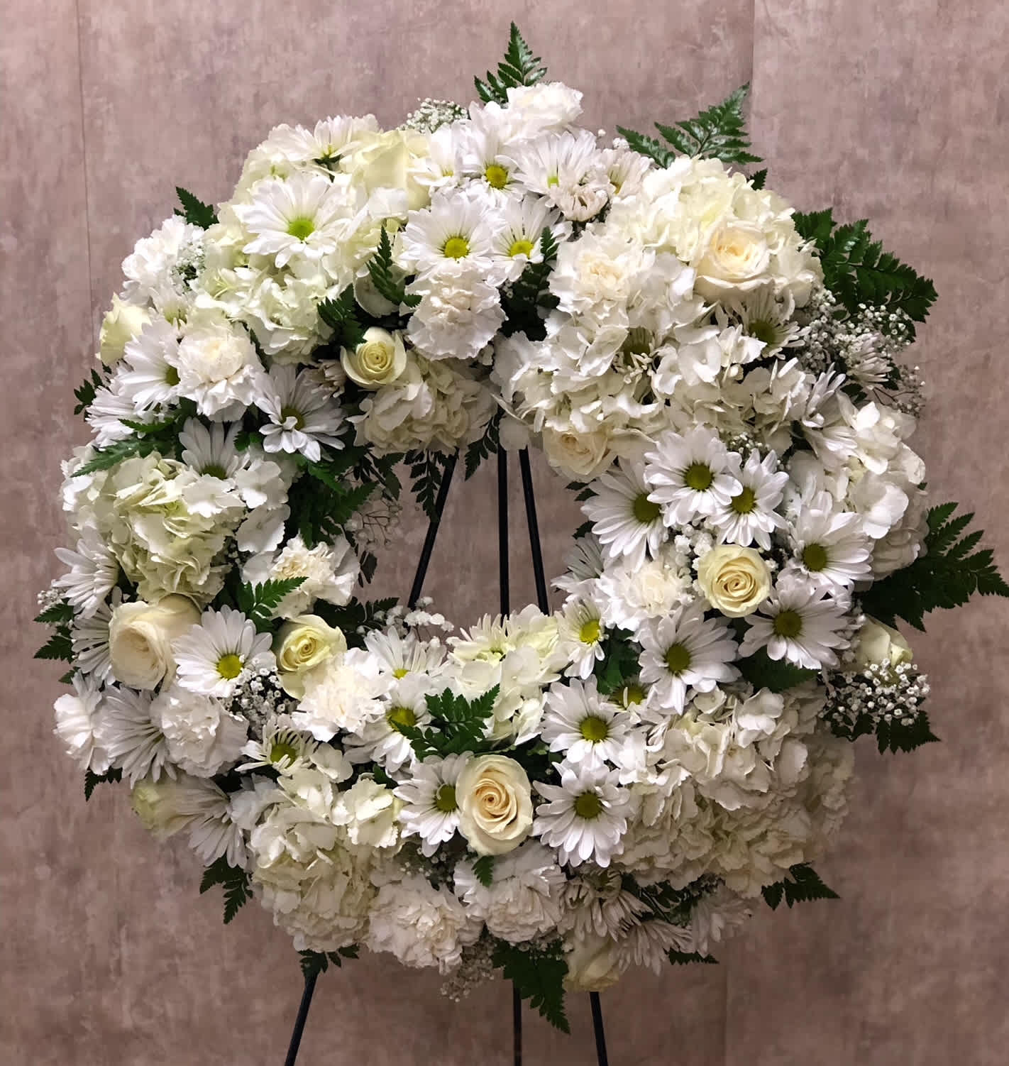Fond Memories (BB) - Celebrate a life well-lived with our exquisite open heart standing spray. This stunning arrangement features a graceful open heart shape, adorned with a delicate mix of white roses, white daisies, white carnations, white hydrangea filler, and lush greenery. It is a symbol of love, purity, and eternal remembrance, offering solace and comfort during times of loss.