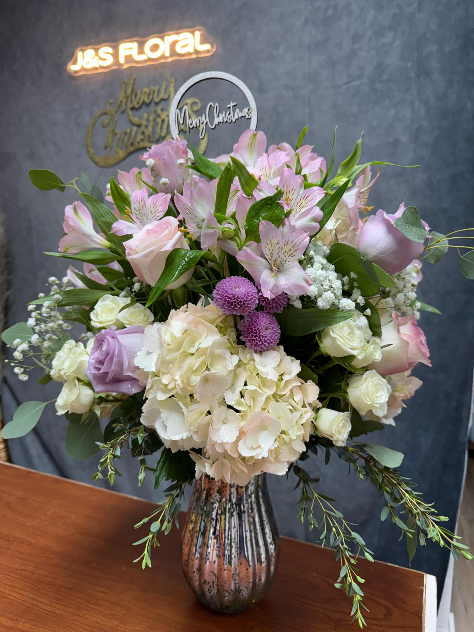 Pink and white floral arrangement in a glass vase with a Christmas topper