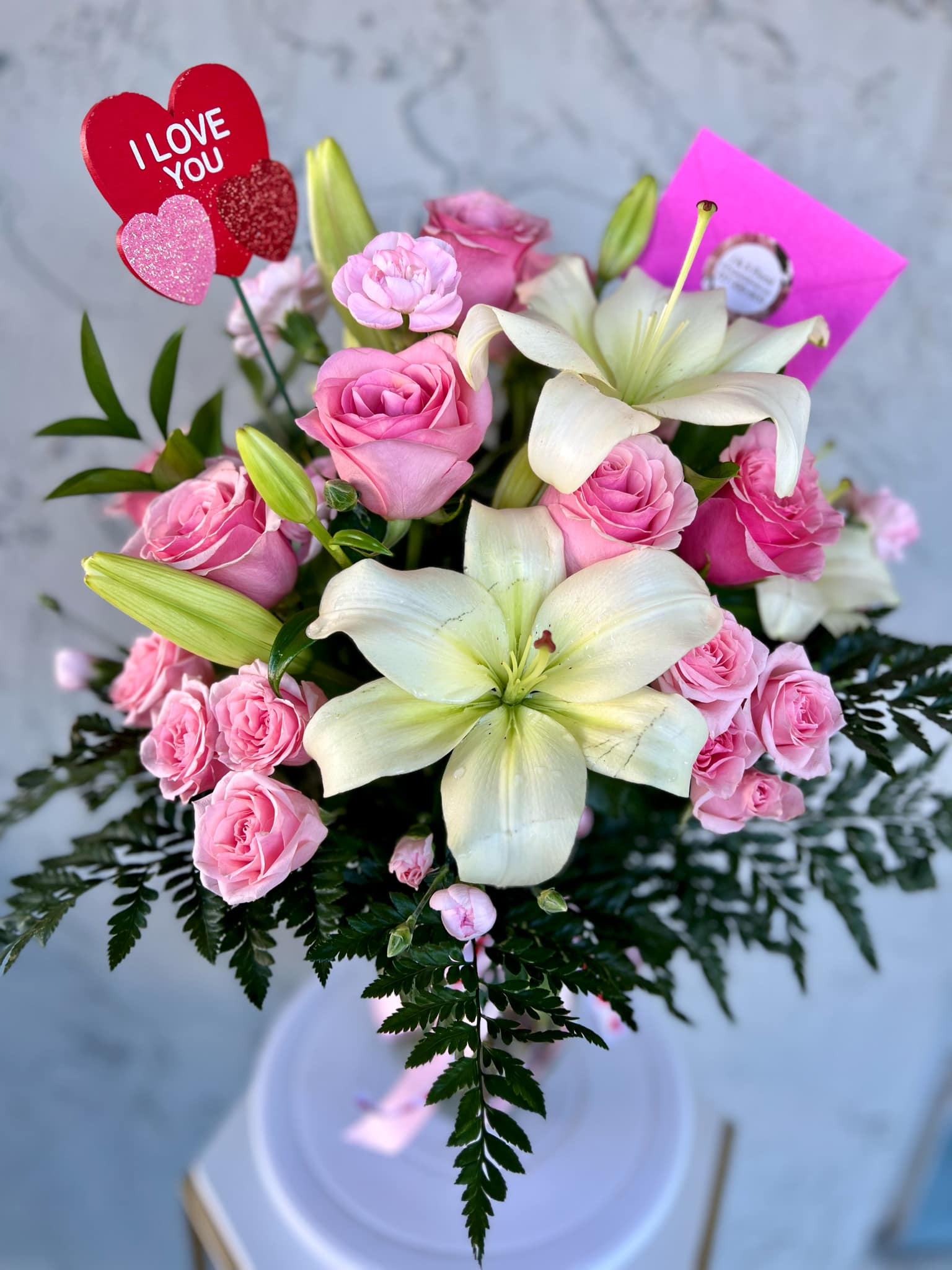 Pink roses and white lilies in a bouquet with an "I LOVE YOU" pick