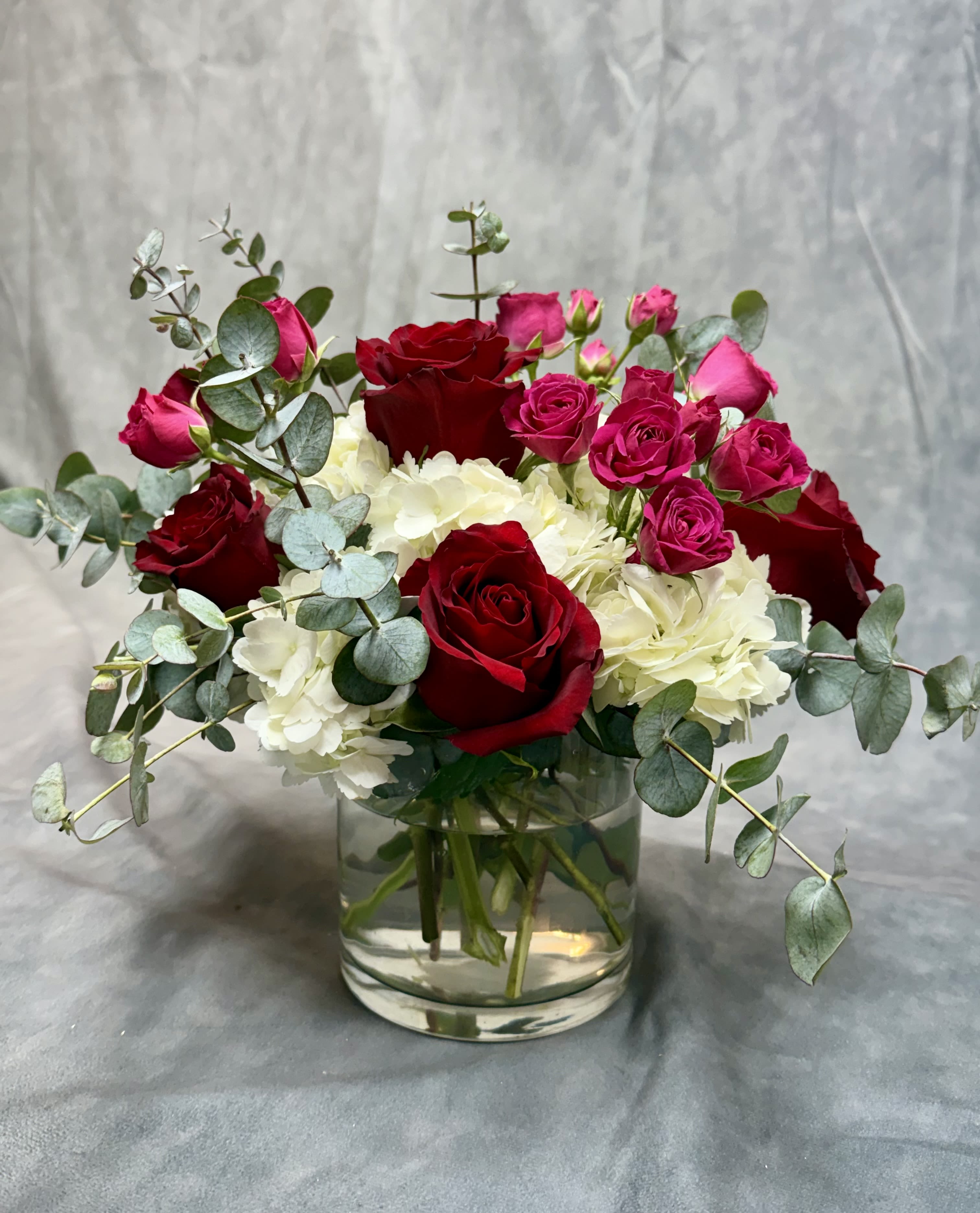 Red and pink roses with white hydrangeas in a glass vase