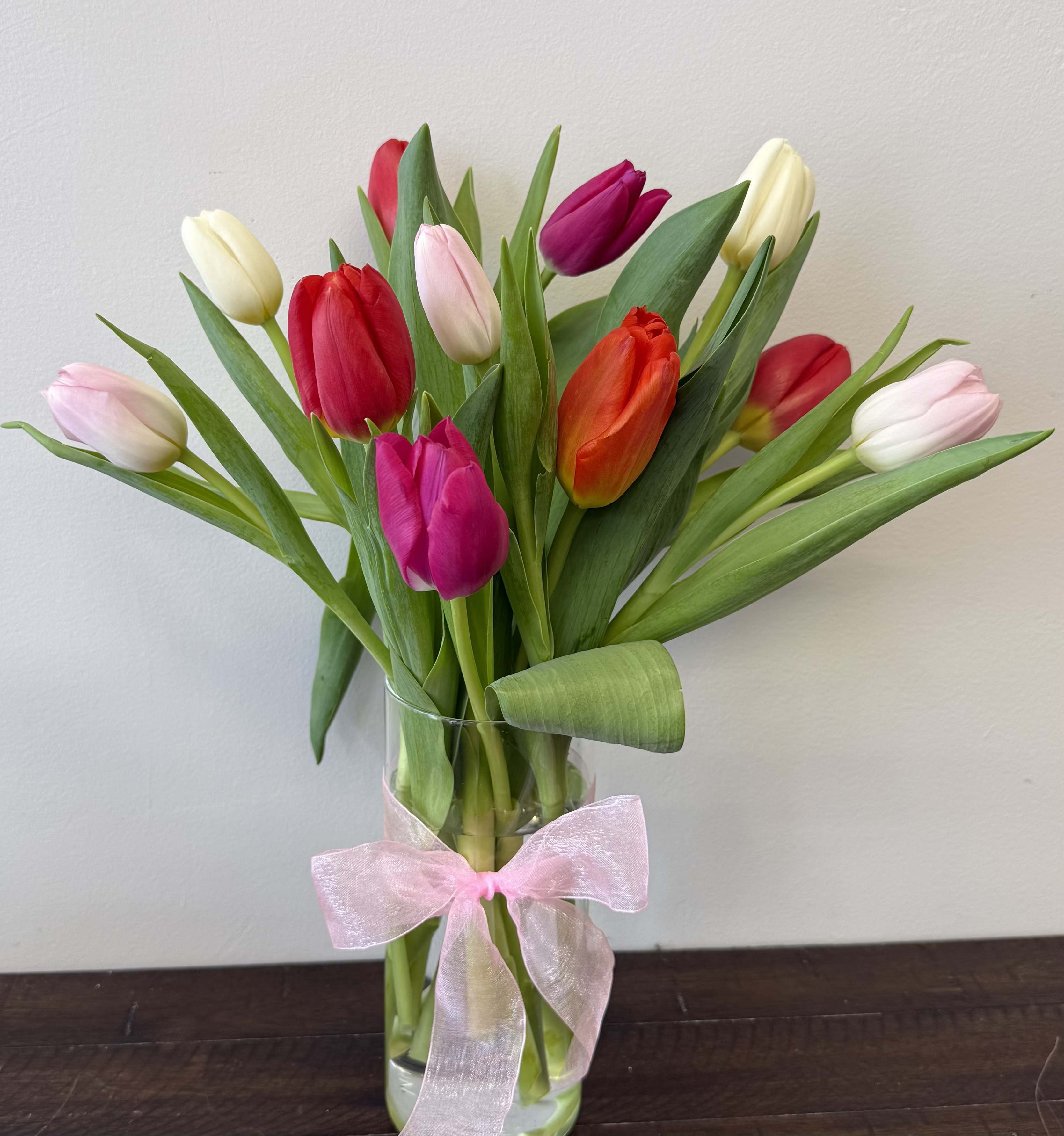 Bouquet of multicolored tulips in a clear glass vase with a pink ribbon