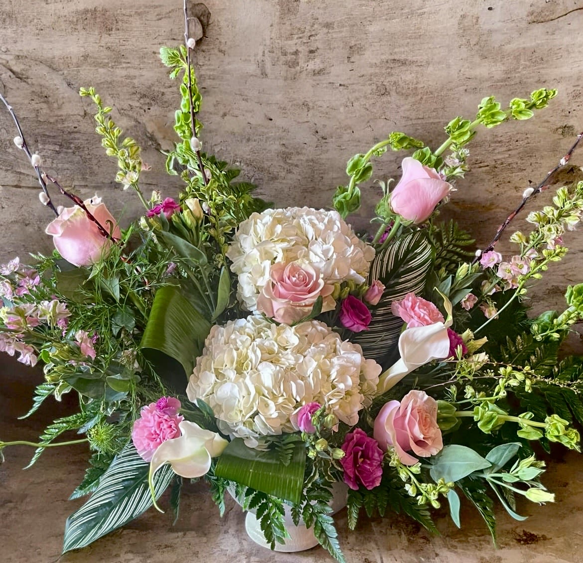 True Enchantment  - This arrangement has roses, bells of Ireland, hydrangea, carnations, Larkspur, aspidistra leaves, pussy willow, Calla  lilies, and greenery. 