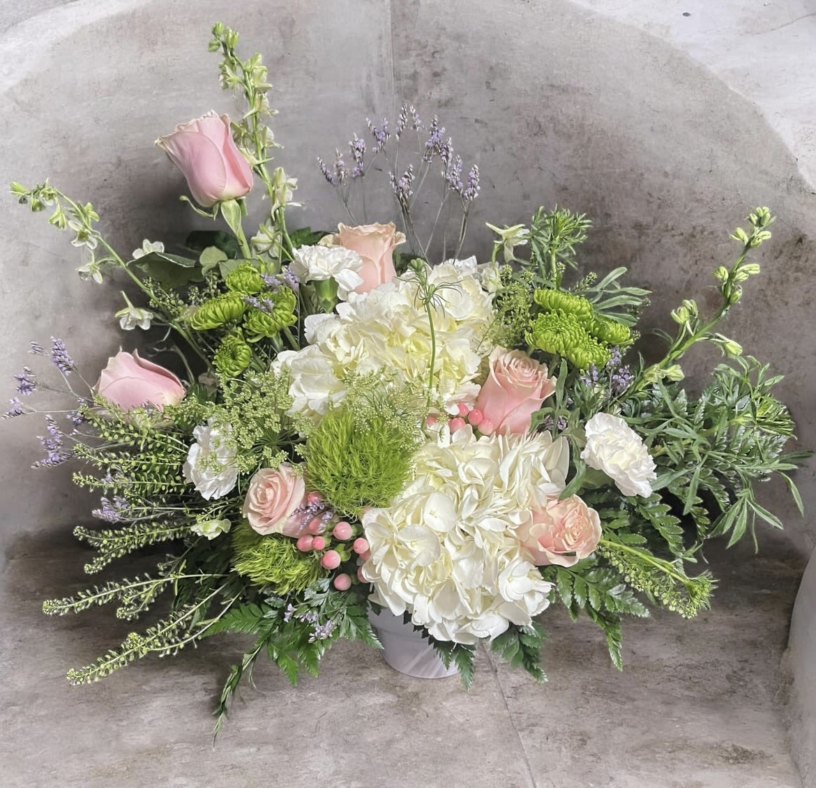 Timeless pastel - Lush pastel mix of roses, hydrangeas, larkspur, hypericum, queen Ann’s lace, trick, misty, carnations, mums and soft filler blooms in a white ceramic container.