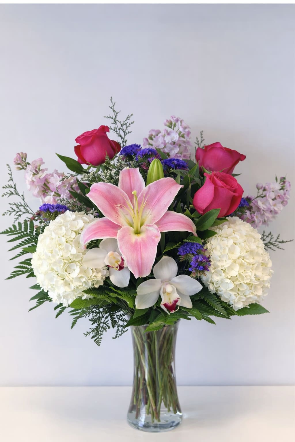 Bouquet of pink roses, lilies, hydrangeas, and orchids in a glass vase