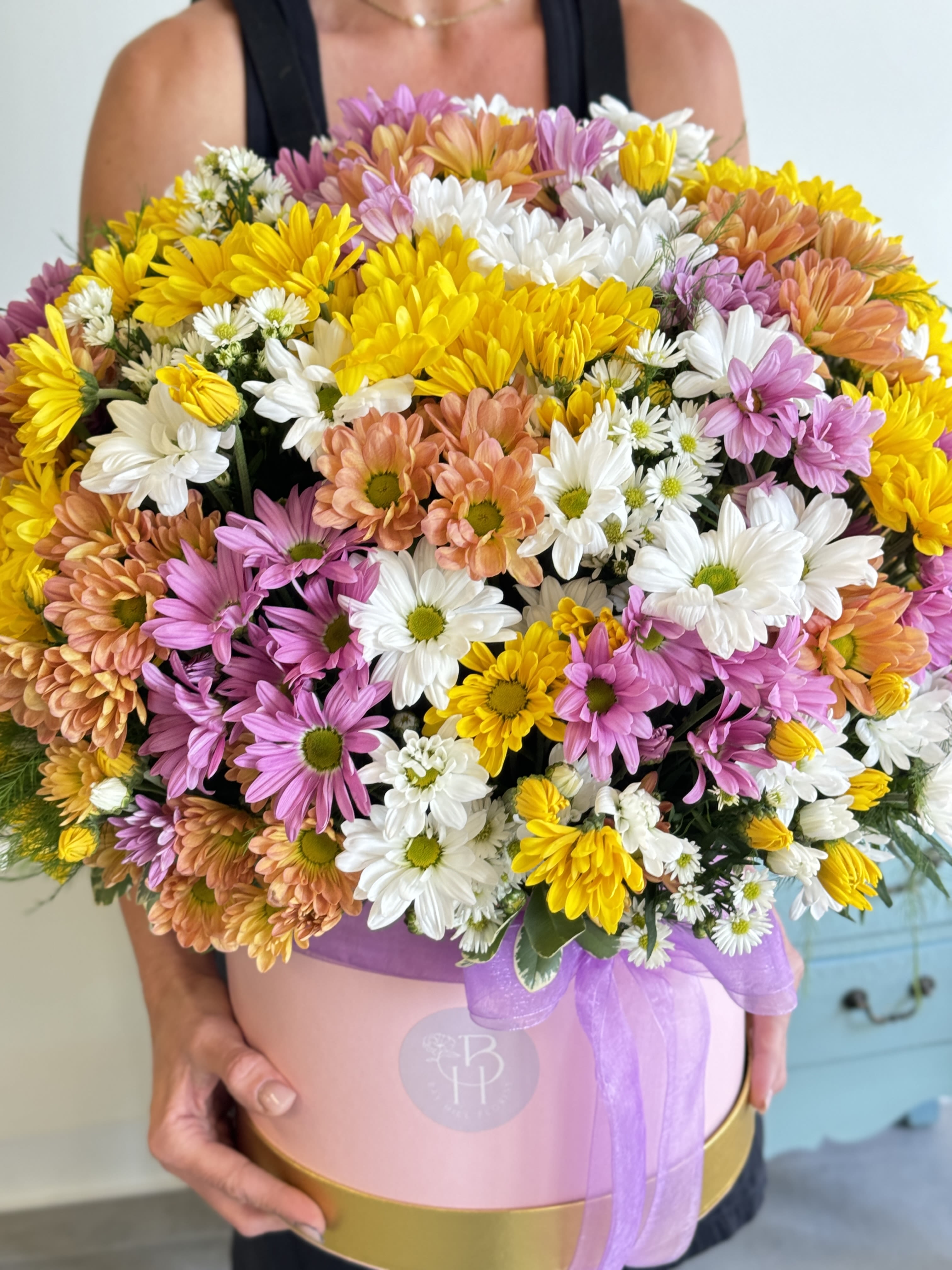 Large mixed daisy bouquet in a pink hat box with a purple ribbon